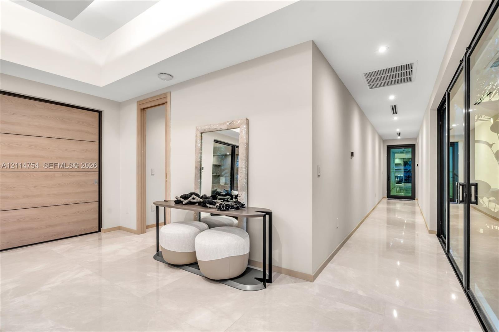 Modern kitchen featuring a waterfall-edge island, stone-surfaced countertops, custom wood-finish cabinetry, floor-to-ceiling black-framed windows, and a multi-pendant light fixture