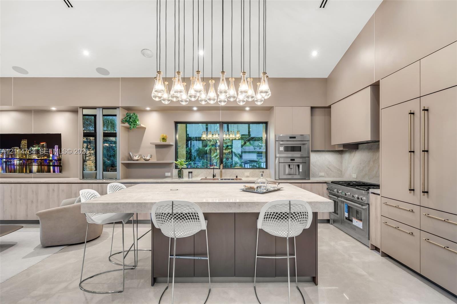 Vaulted ceilings, extensive custom cabinetry with light wood-finish detailing, recessed lighting, multi-light linear pendant fixture, and large-format tile flooring
