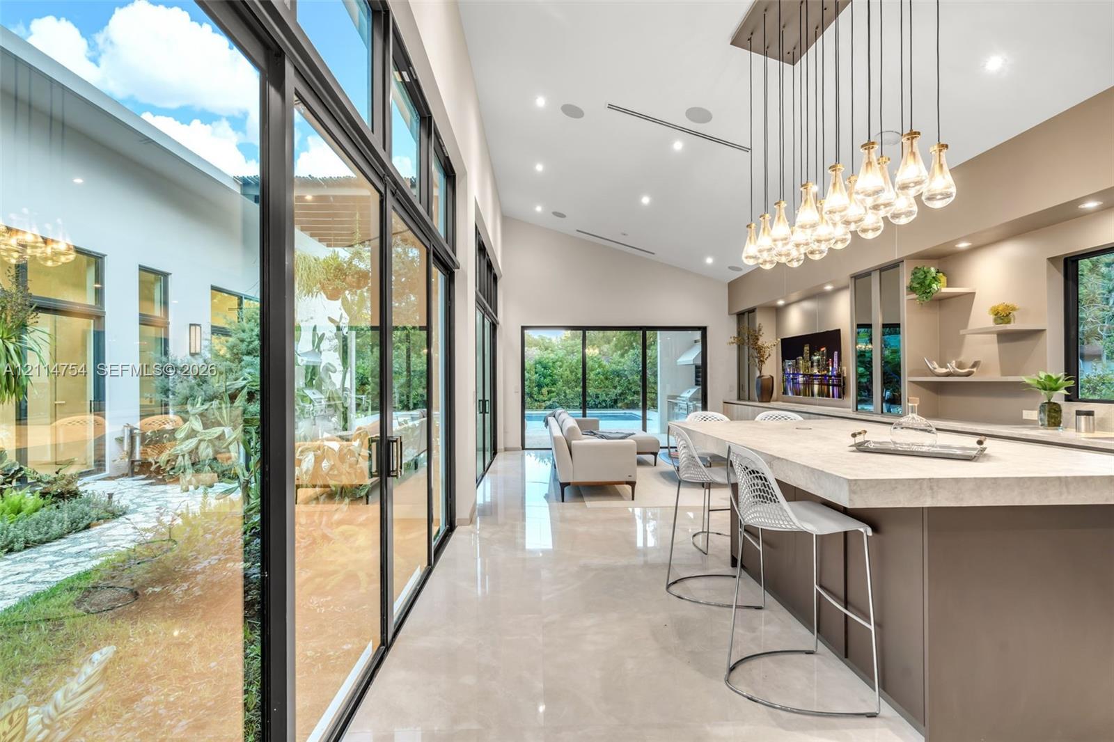Vaulted ceilings with recessed lighting, full-height glass sliding doors, large-scale crystal and metal chandelier, built-in cabinetry with natural stone countertop, and polished tile flooring