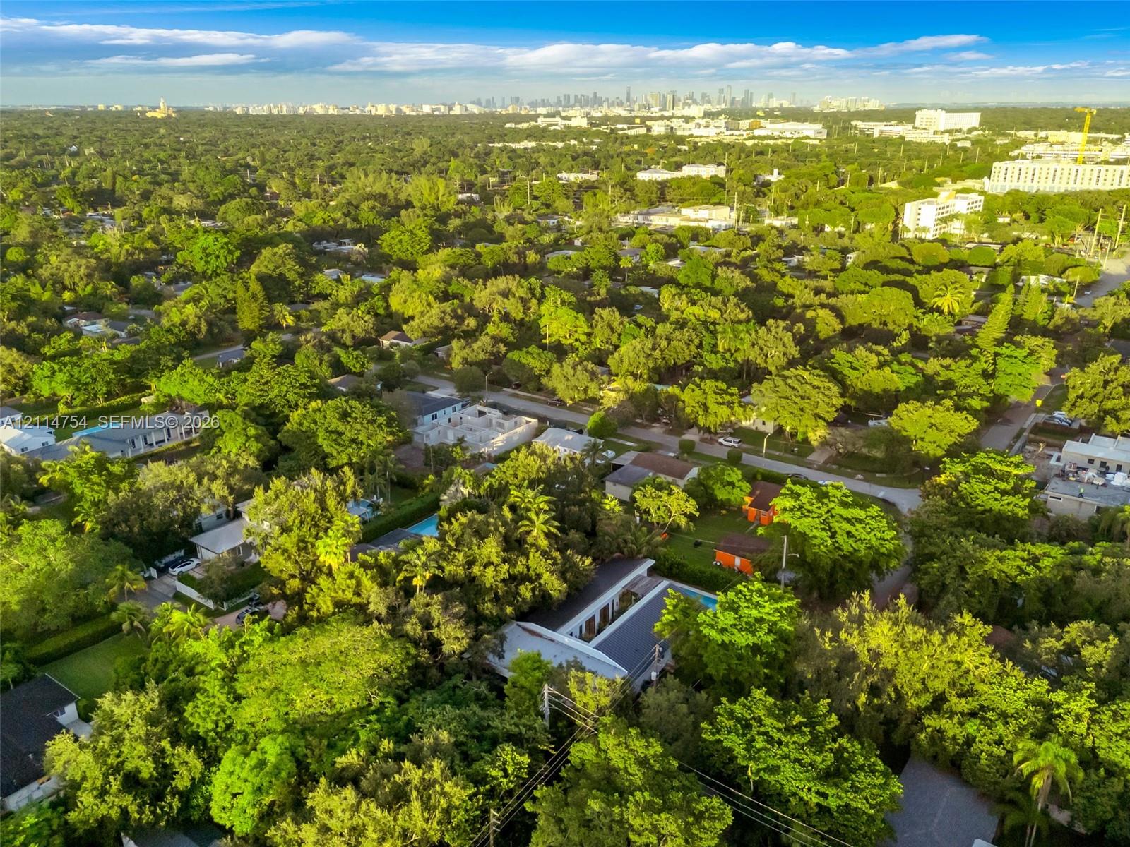 Aerial perspective of a detached residential property featuring a flat roofline, central skylight structure, and a backyard swimming pool, set within a heavily wooded lot