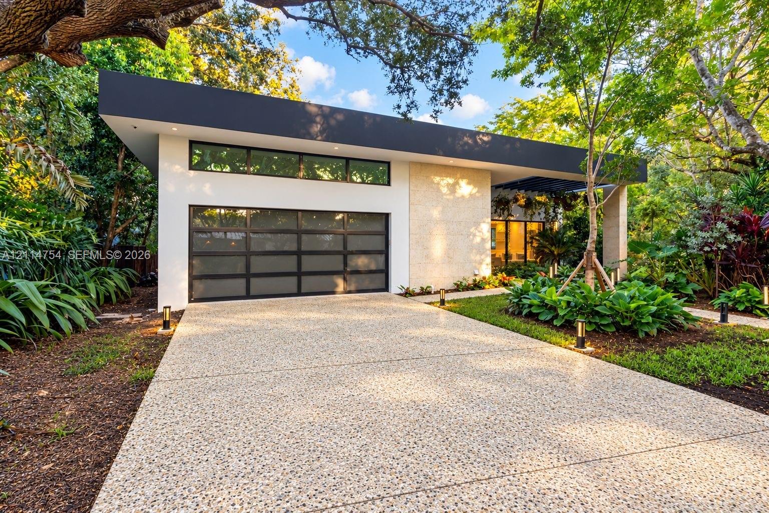 Expansive open-concept living area featuring a recessed tray ceiling with integrated cove lighting, polished stone flooring, custom built-in cabinetry with floating shelving, and floor-to-ceiling glass panel doors