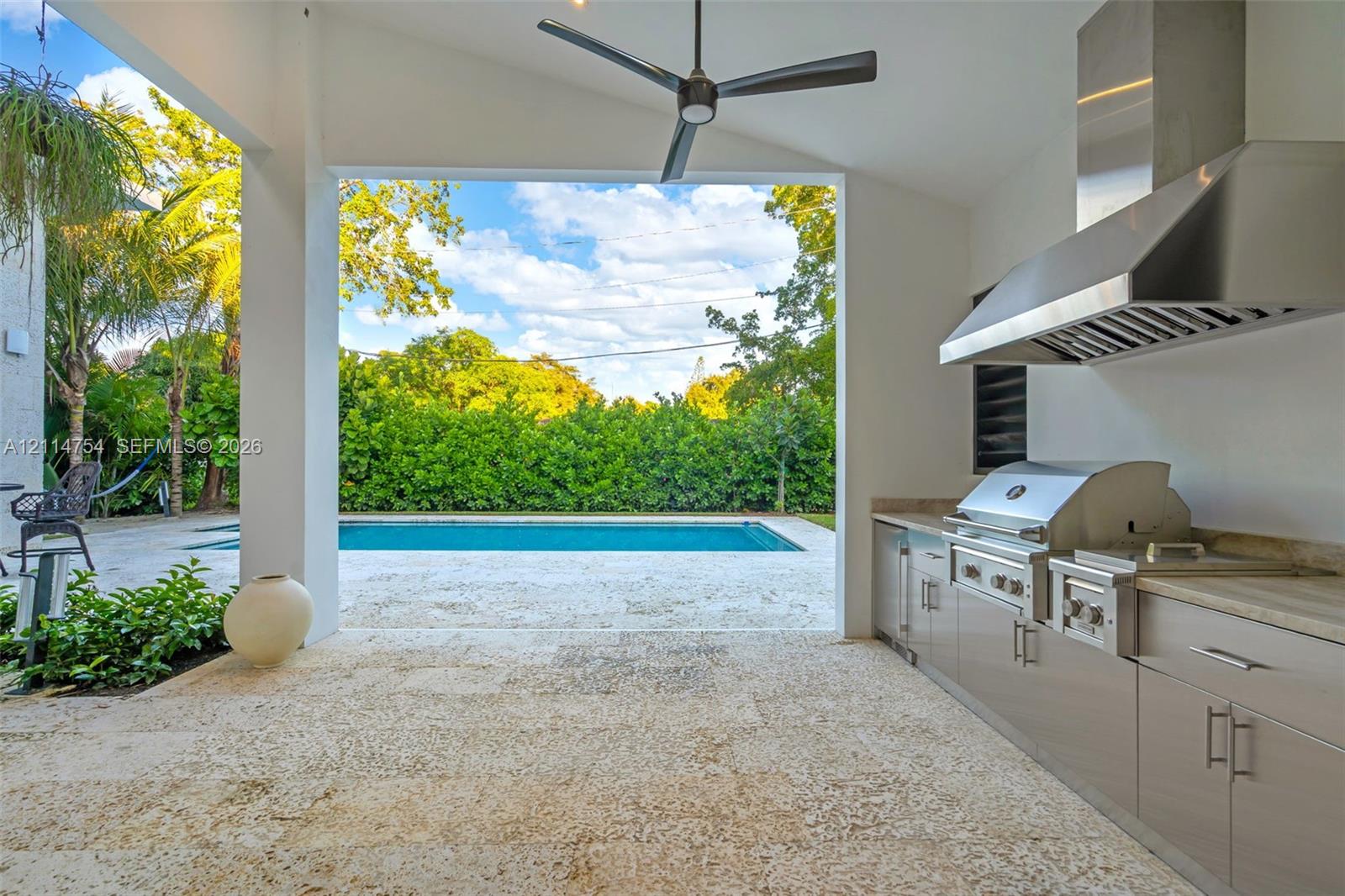 Covered patio featuring stone tile flooring, stainless steel outdoor kitchen with built-in grill, stone countertop, ceiling fan, and expansive sliding glass doors