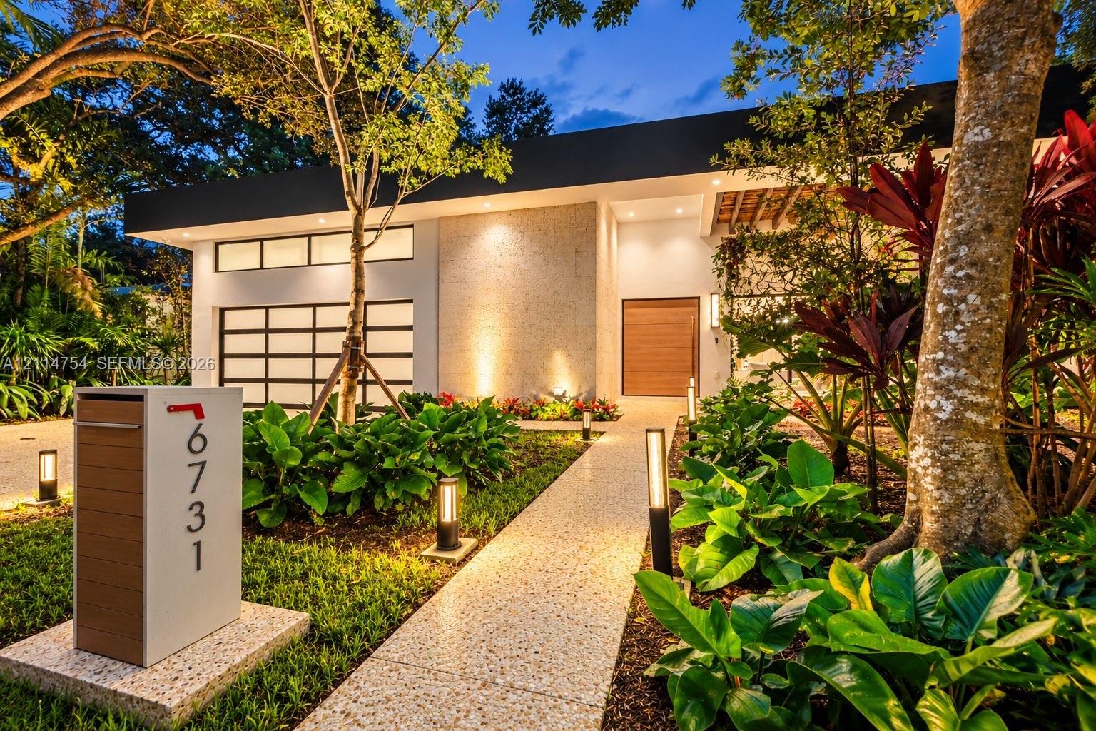 Pivot entry door featuring a light-toned wood finish and a long cylindrical metal handle, textured stone exterior wall, vertical wall-mounted exterior light fixture, and polished stone tile flooring