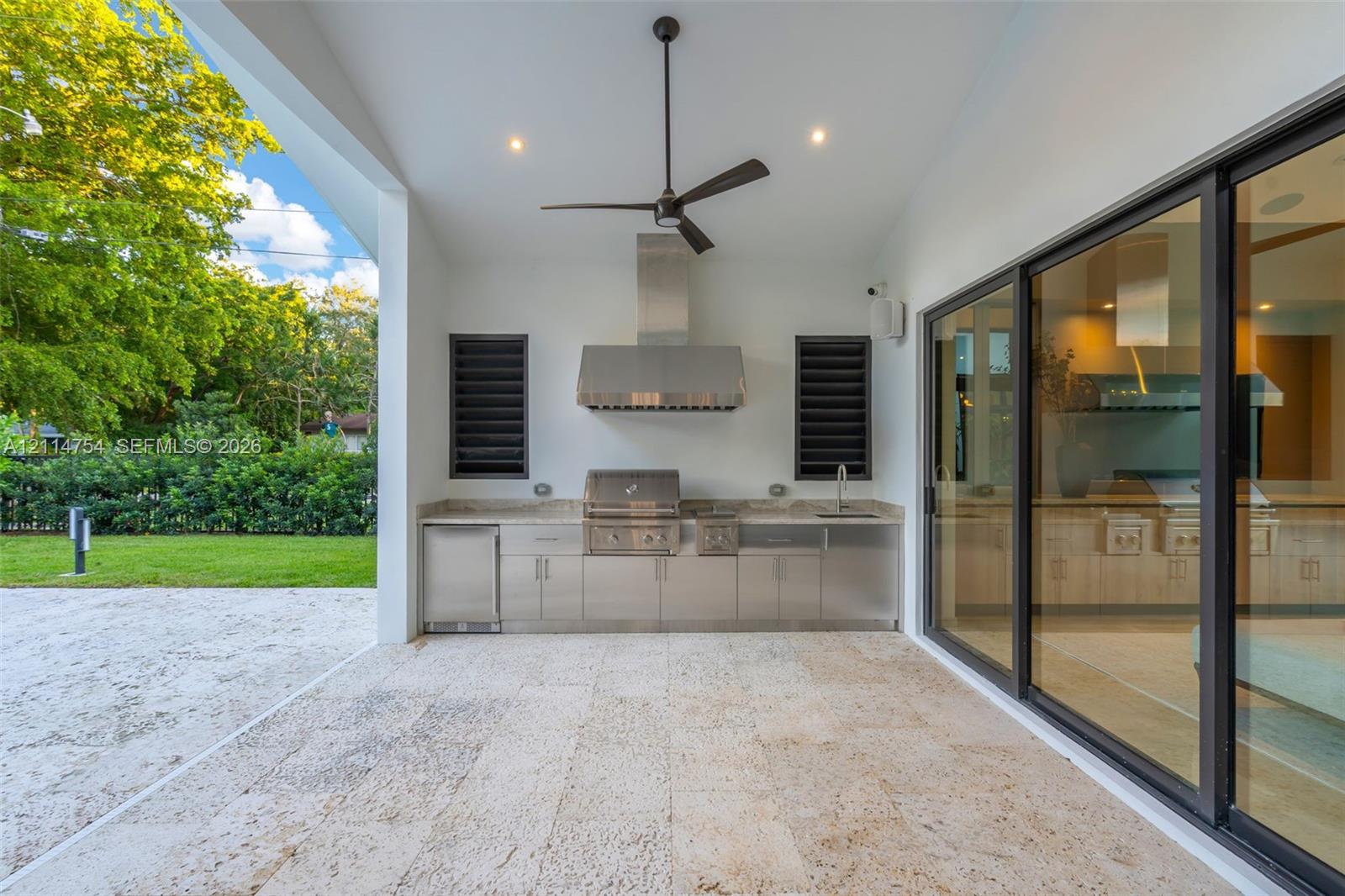 Covered patio featuring stone tile flooring, stainless steel outdoor kitchen with built-in grill, stone countertop, ceiling fan, and expansive sliding glass doors