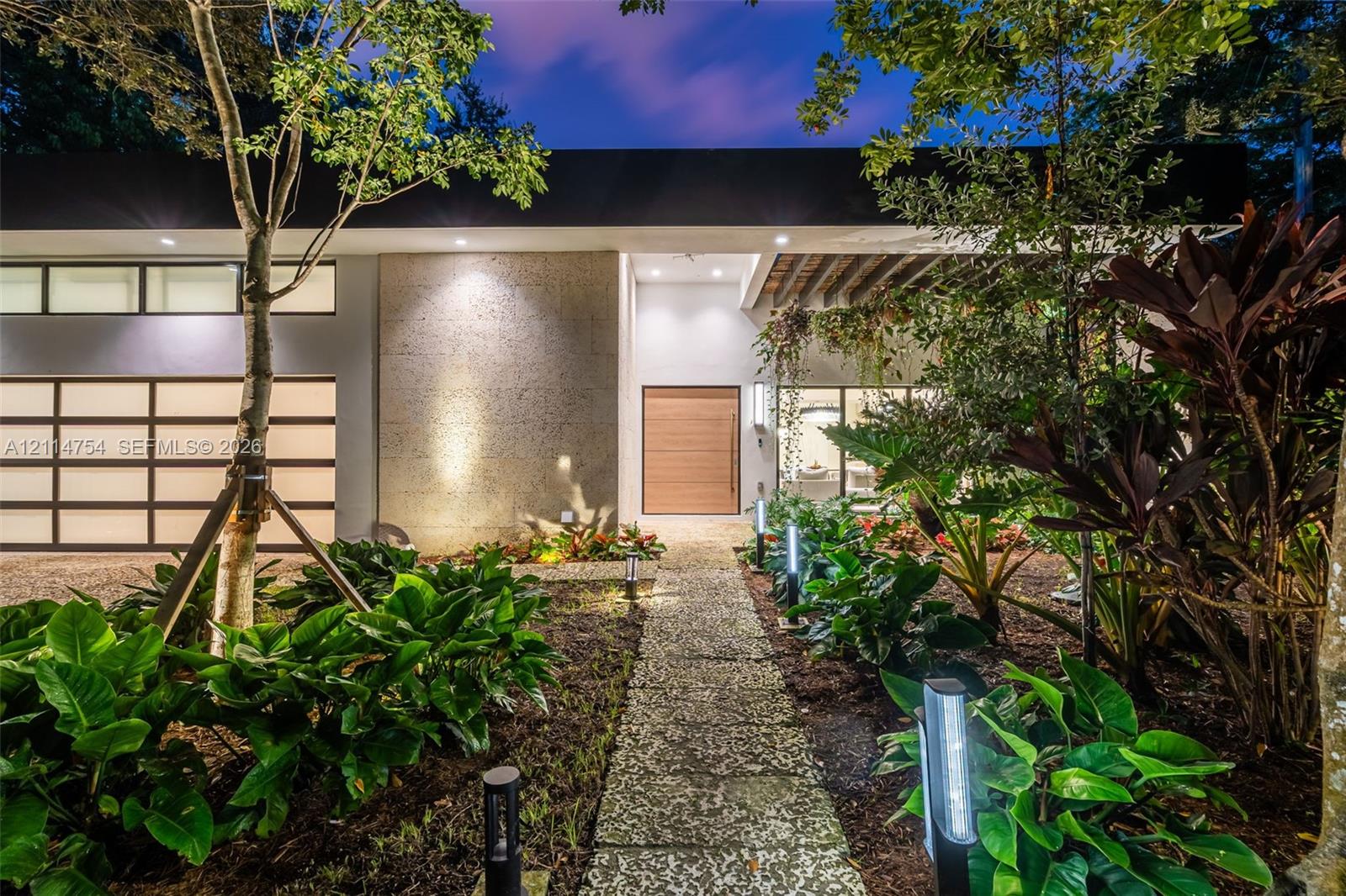 Modern exterior featuring a flat roofline, clerestory windows, a multi-panel glass garage door, a natural wood entry door, and a stone-paver walkway