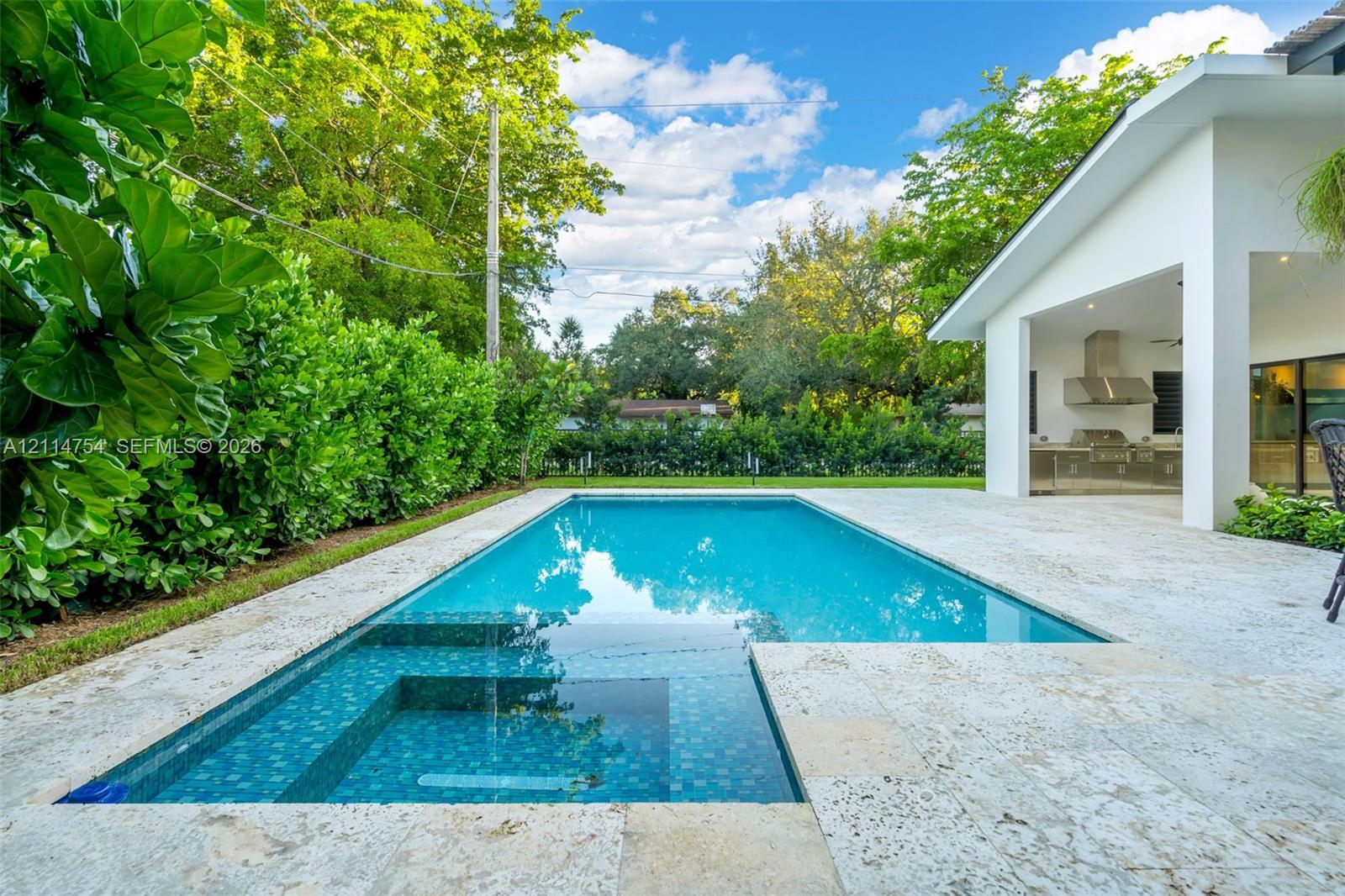 Swimming pool with stone-tiled decking, covered patio with integrated ceiling fan, and exterior wall cladding