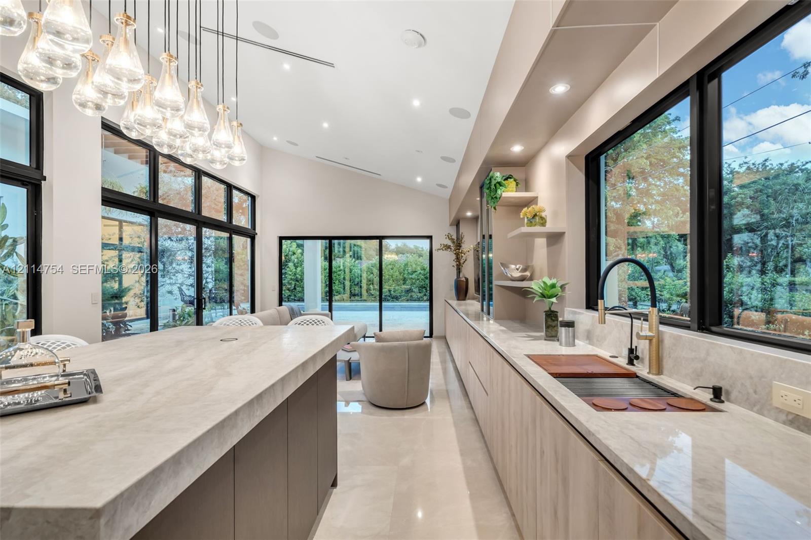 Vaulted ceilings with recessed lighting, floor-to-ceiling multi-panel glass doors, custom wall-to-wall cabinetry with stone countertops, and integrated ceiling speakers