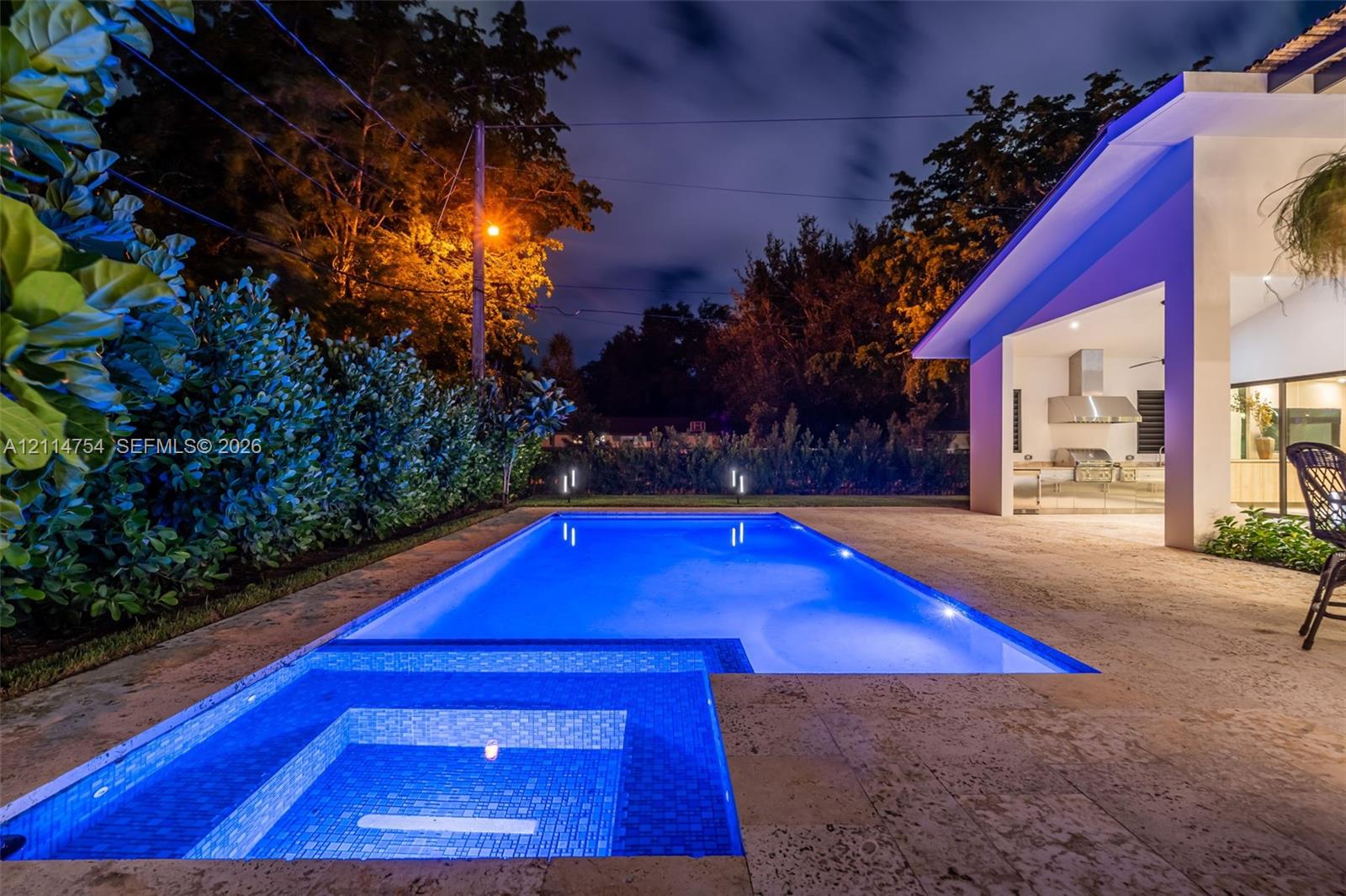 In-ground swimming pool with stone deck, covered patio, integrated pergola, and sliding glass wall systems