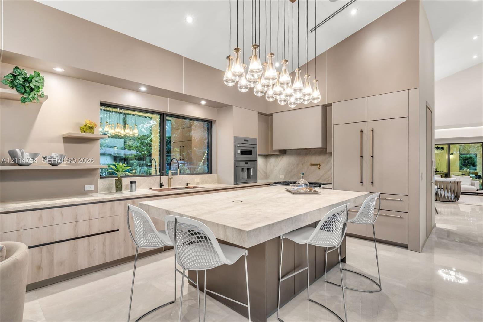 Kitchen featuring flat-panel cabinetry, a large stone-topped central island, built-in stainless steel appliances, and a multi-pendant light fixture beneath a vaulted ceiling