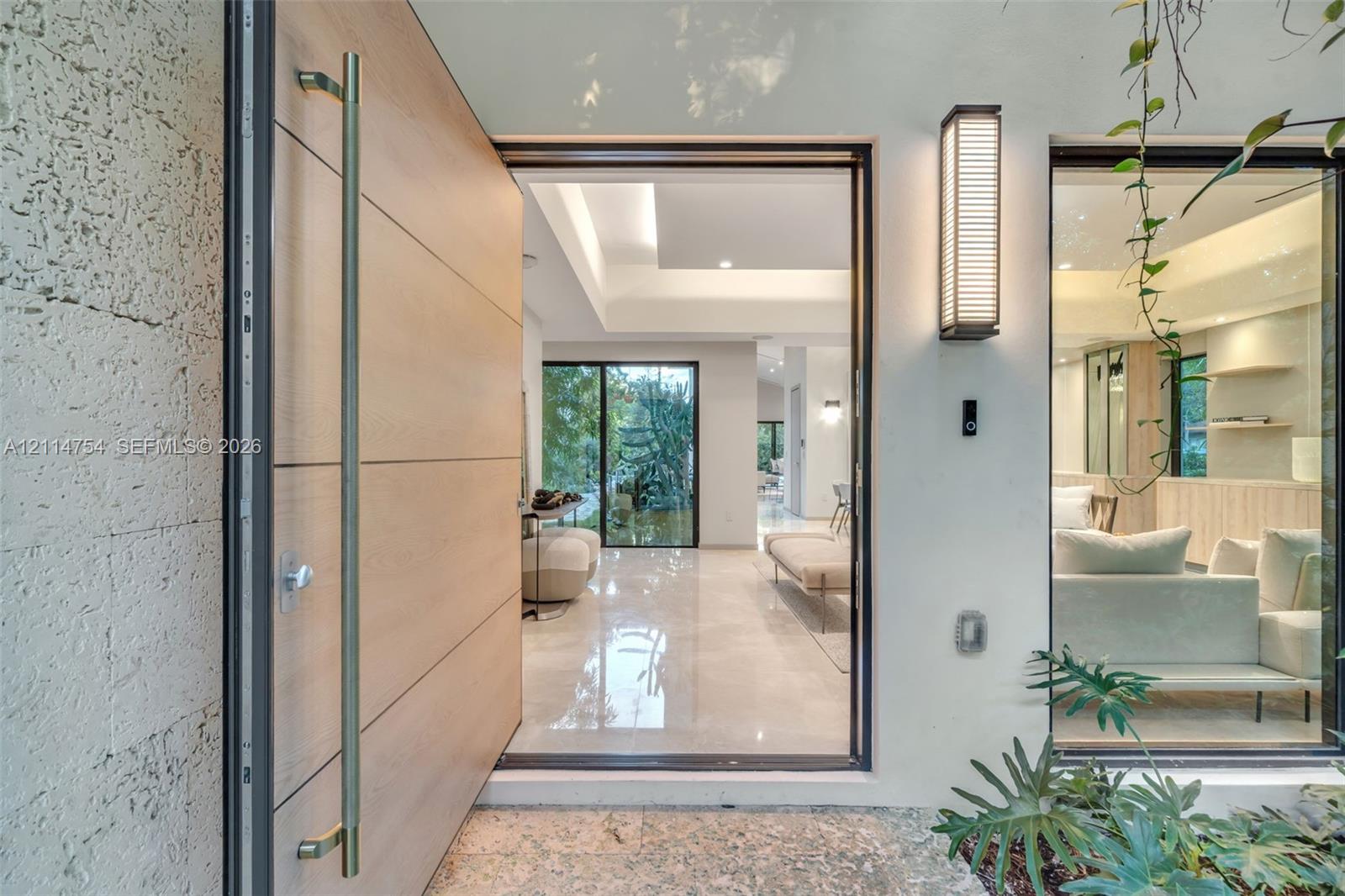 Tray ceiling with cove lighting, expansive floor-to-ceiling glass paneling, polished stone flooring, custom built-in cabinetry with floating shelving, and large-format wood-finish entry door
