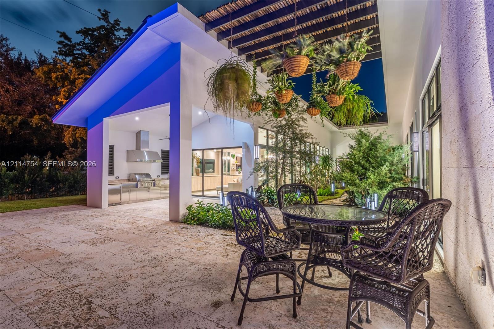 Modern swimming pool featuring stone deck surround, covered outdoor kitchen with stainless steel appliances, and a wood-slat overhead pergola