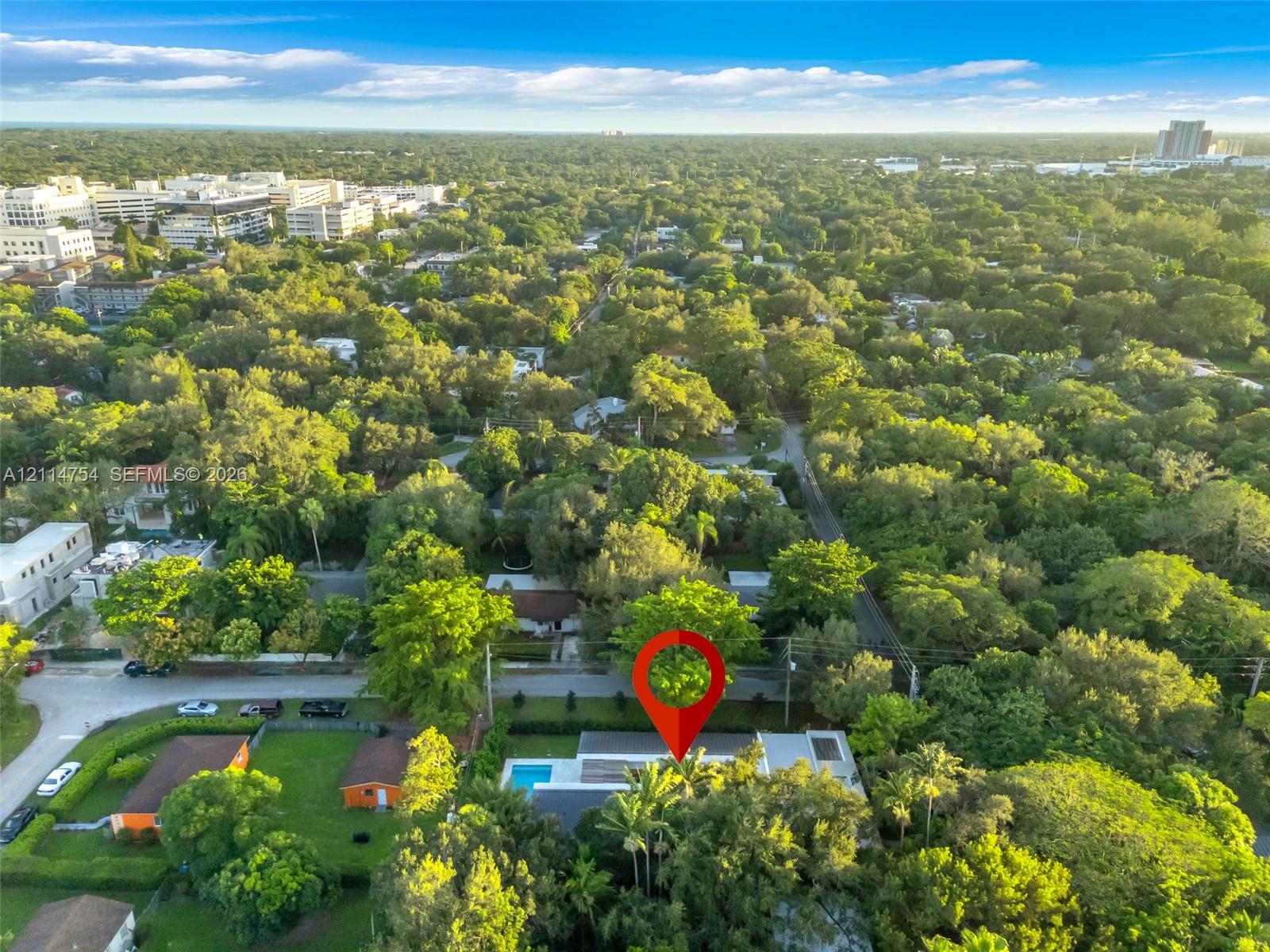 Aerial perspective of a property featuring a private swimming pool, flat roofline, paved patio, and dense mature perimeter landscaping