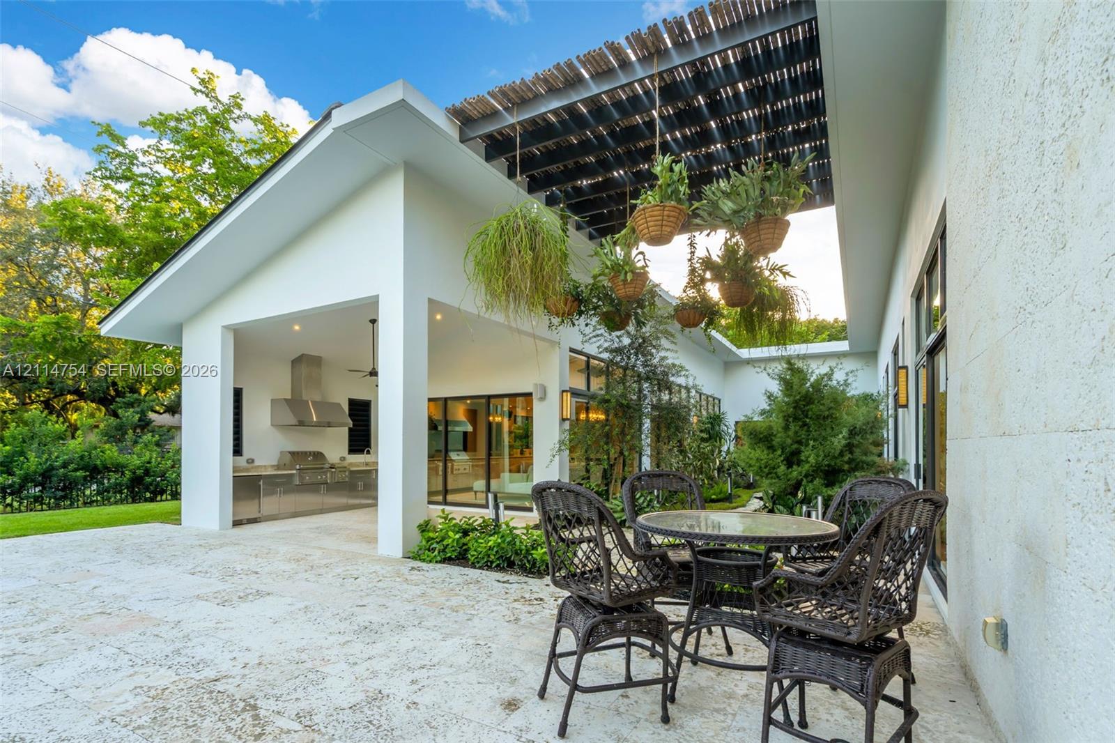 In-ground swimming pool with tiled border, expansive stone-paved patio, covered outdoor kitchen with stainless steel appliances, and minimalist white exterior siding