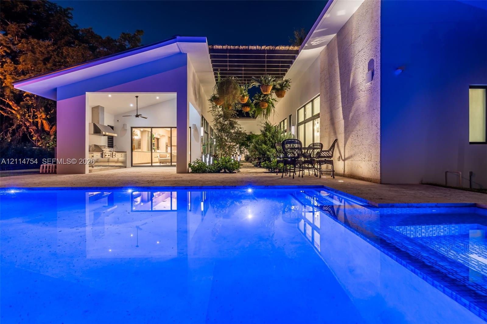 Rectangular in-ground pool with stone-finish decking, covered patio with structural pergola, and expansive glass sliding door panels