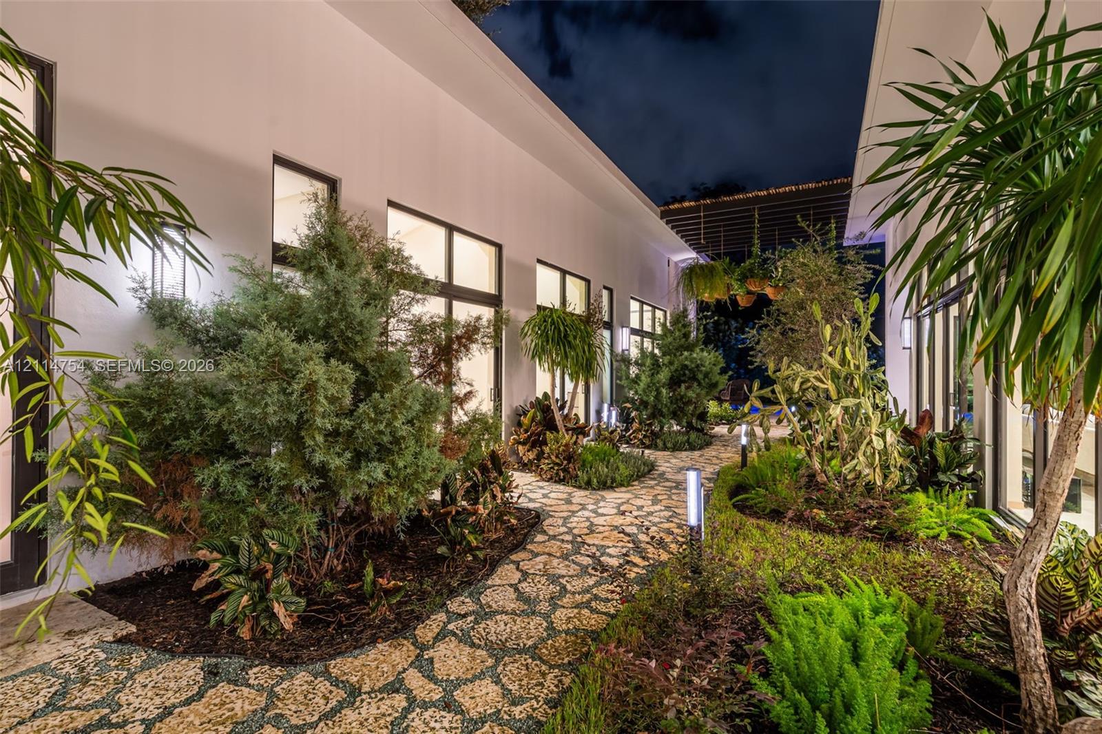 Covered outdoor patio featuring stone flooring, a slatted timber pergola, and a built-in outdoor kitchen with a stainless steel range hood
