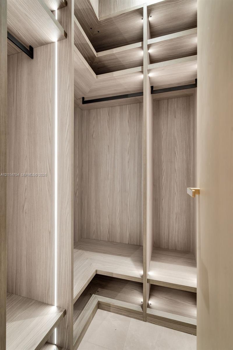 Walk-in shower with vertical stone-finish tiling, brass-toned rainfall shower head, wall-mounted vanity with integrated sink, and illuminated mirrored medicine cabinet