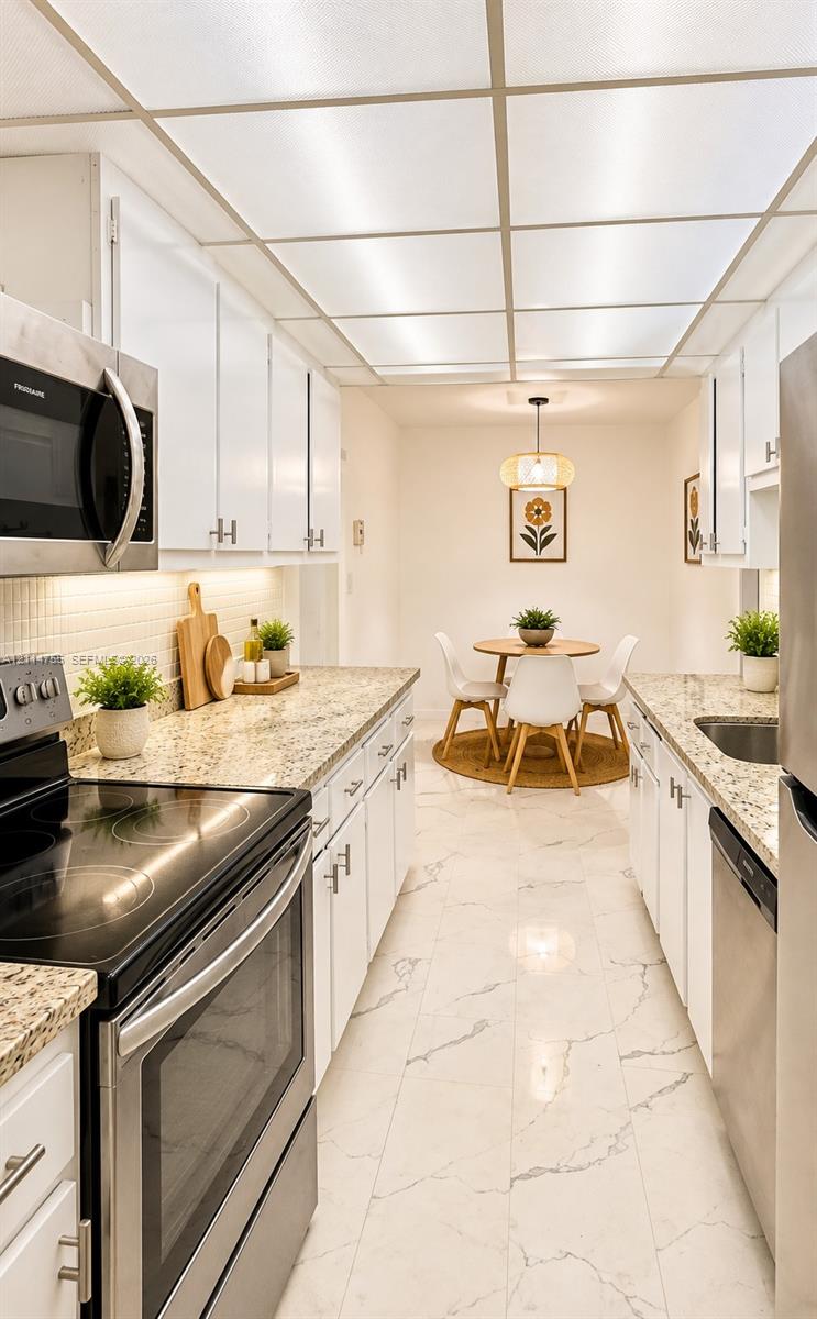 Kitchen featuring stone countertops, stainless steel appliances, white cabinetry with silver-tone hardware, and large-format tile flooring