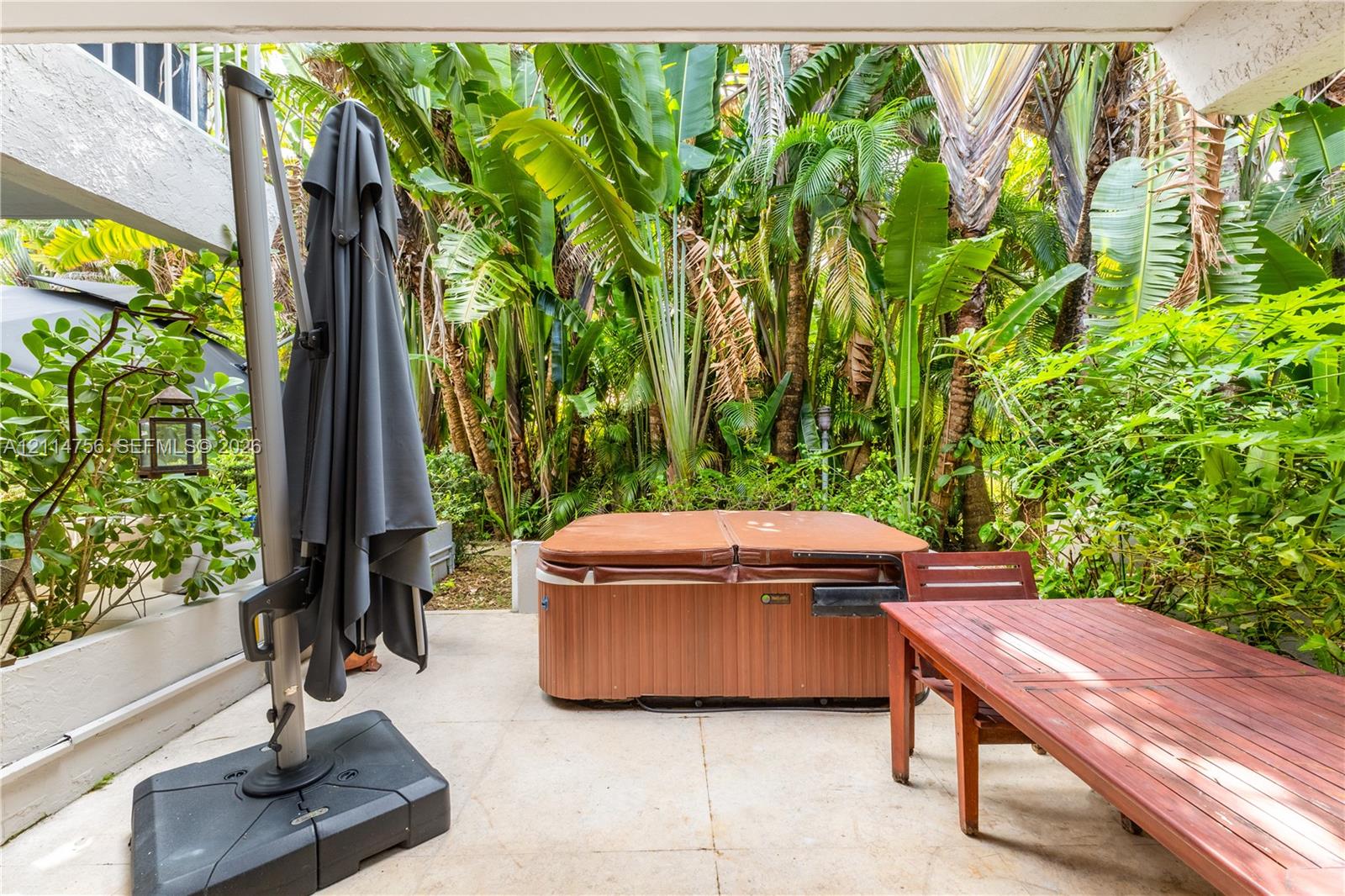 Outdoor patio featuring light-toned stone tile flooring, a built-in spa, and established tropical vegetation