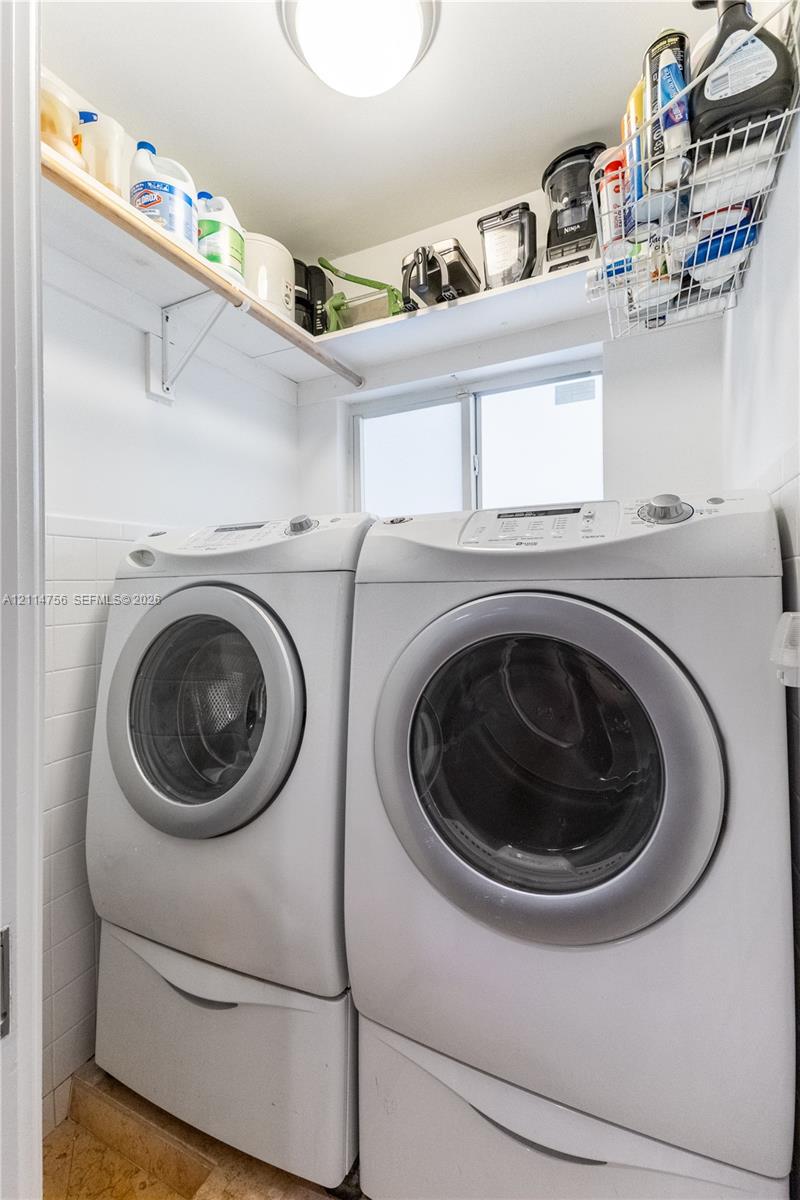 Laundry area featuring white subway tile wall cladding, fixed upper wood shelving, an operable window, and a flush-mount ceiling light fixture