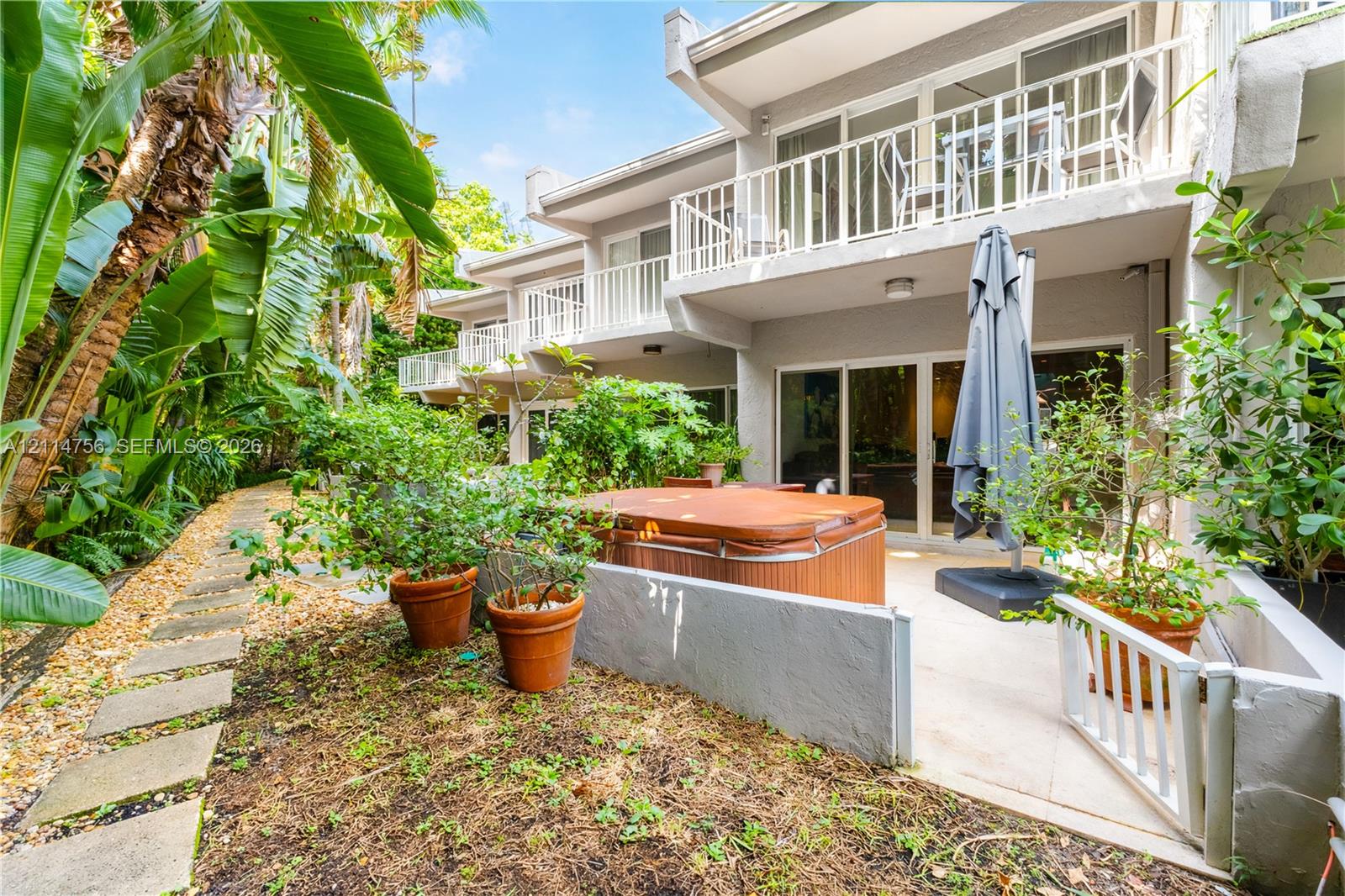 Concrete patio featuring built-in low wall enclosures, multi-level balconies with white railings, and a concrete paver walkway