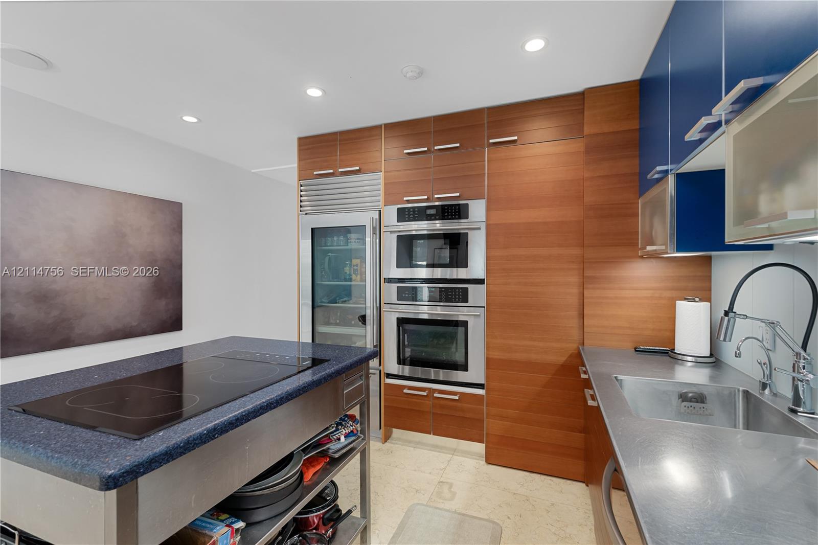 Kitchen featuring wood-finish cabinetry, built-in stainless steel double oven, integrated refrigeration, metal countertop with a sink, and a central island with an induction cooktop