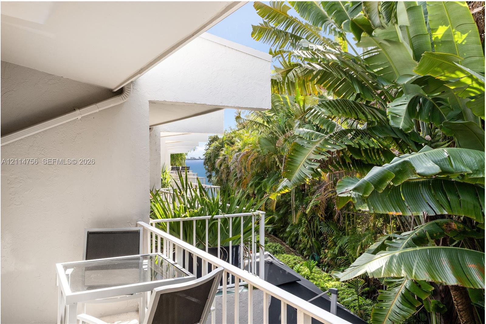 Covered balcony featuring white metal railings and mature tropical landscaping