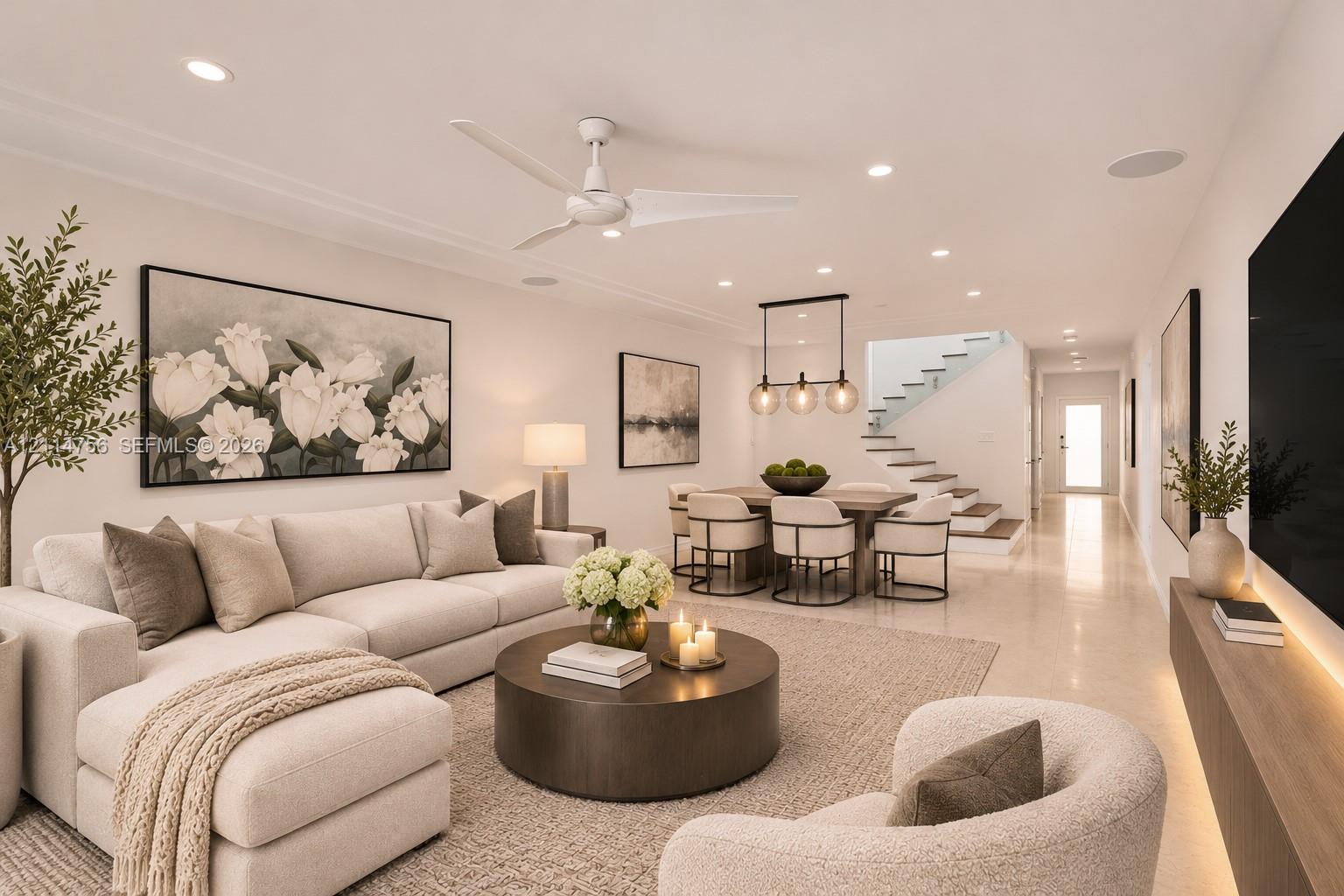 Open-concept interior featuring light-toned flooring, recessed ceiling lighting, a contemporary three-blade ceiling fan, a linear wood-finish wall-mounted media console with integrated lighting, and a staircase with glass railings Open-concept interior featuring light-toned flooring, recessed ceiling lighting, a contemporary three-blade ceiling fan, a linear wood-finish wall-mounted media console with integrated lighting, and a staircase with glass railings