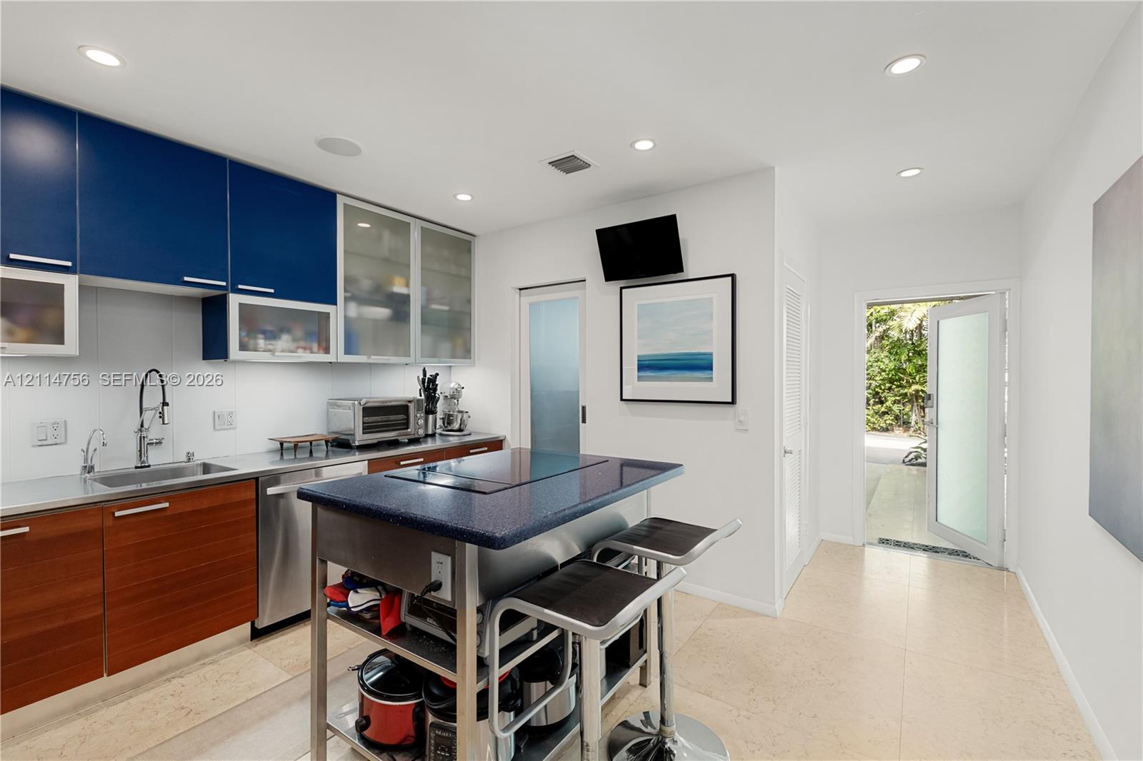 Kitchen featuring dual-tone cabinetry, stainless steel sink with high-arc faucet, central island with integrated cooktop, stone countertop surfaces, and recessed lighting