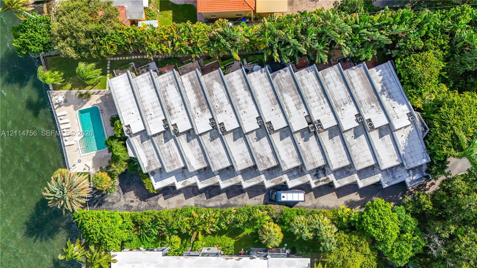 Aerial perspective of a multi-unit property featuring a waterfront swimming pool, paved pool deck, and mature landscaping
