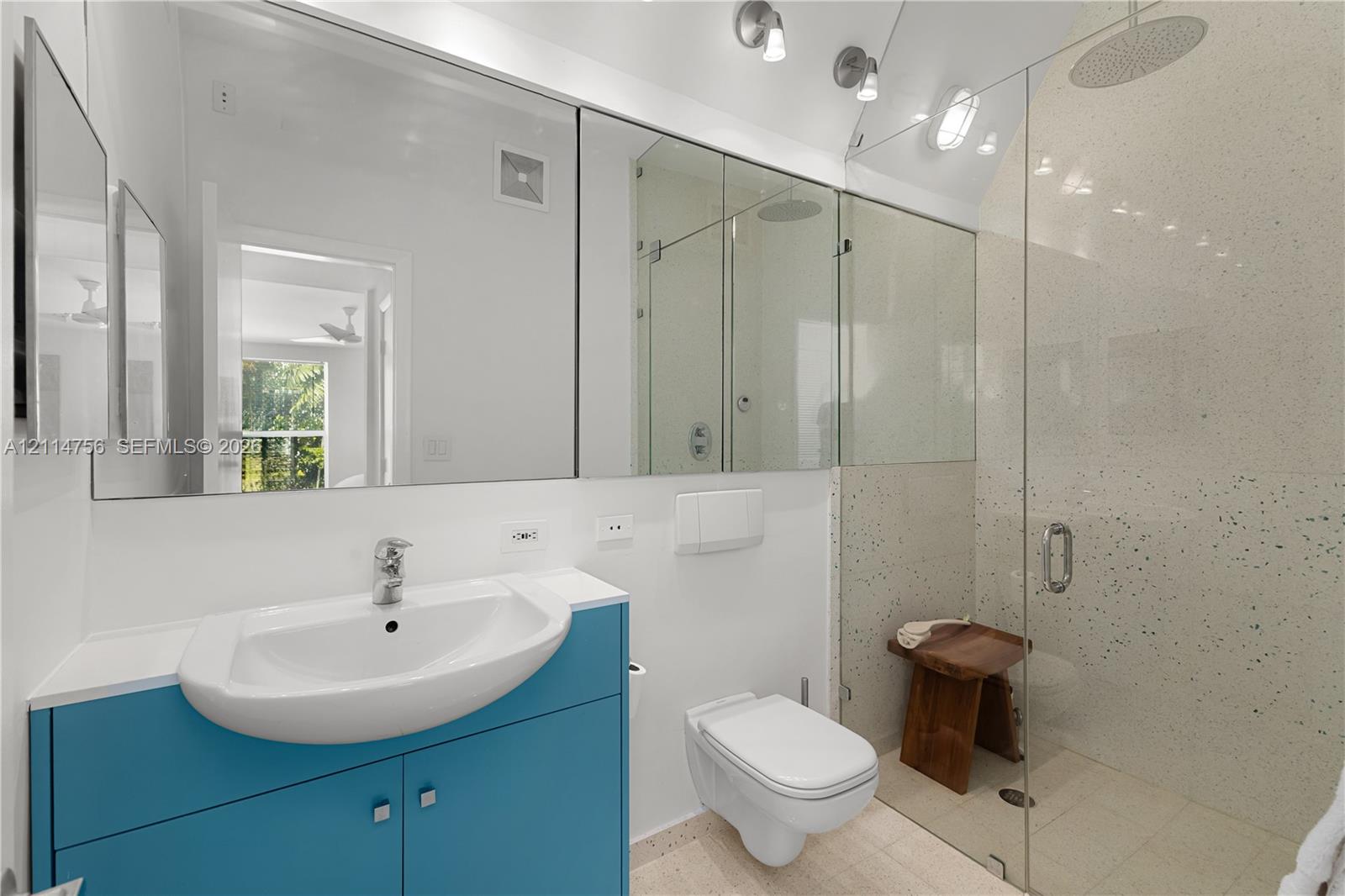 Floating vanity with a porcelain sink, wall-mounted toilet, walk-in shower with a frameless glass enclosure, rain-style showerhead, and expansive mirror