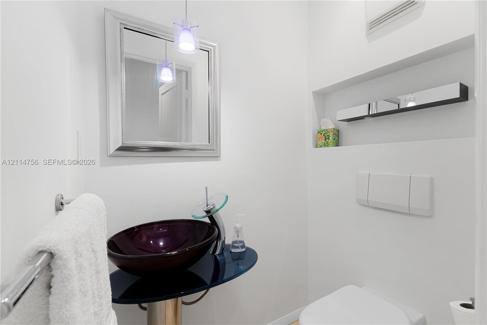 Floating vanity with a dark-tinted glass countertop, circular vessel sink, chrome-finish faucet, wall-mounted mirror, and recessed wall shelving