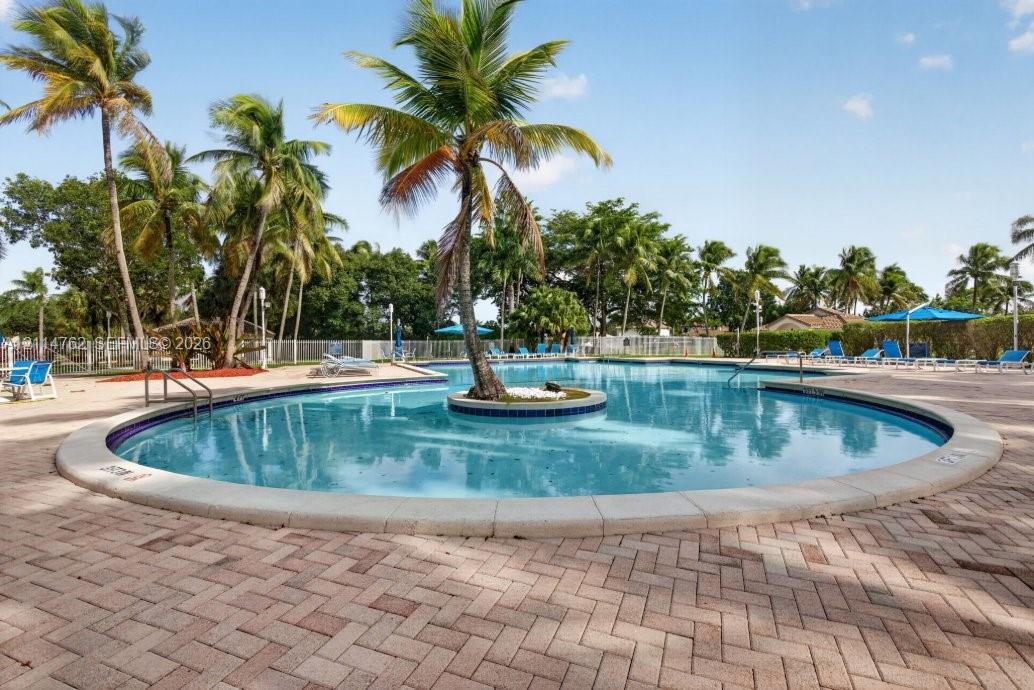 In-ground swimming pool featuring a central island with a palm tree, stone-paver decking, and metal pool safety fencing