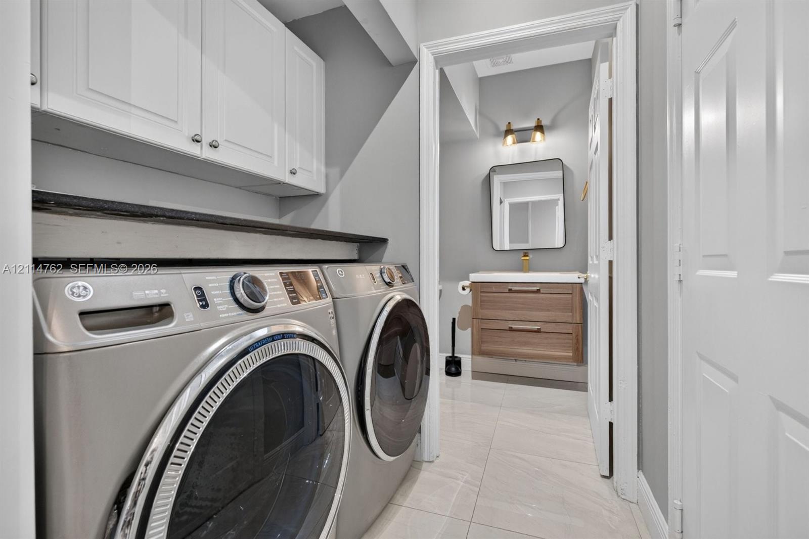 Laundry area featuring white shaker-style wall cabinets and a solid-surface countertop