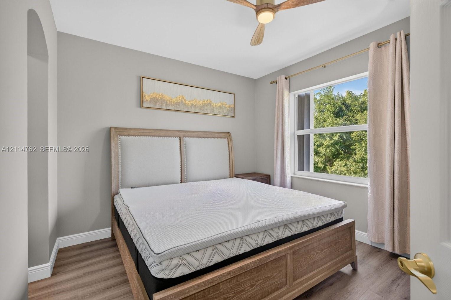 Neutral wall tones with wood-finish flooring, recessed ceiling fan with wood-tone blades, and large window with natural light
