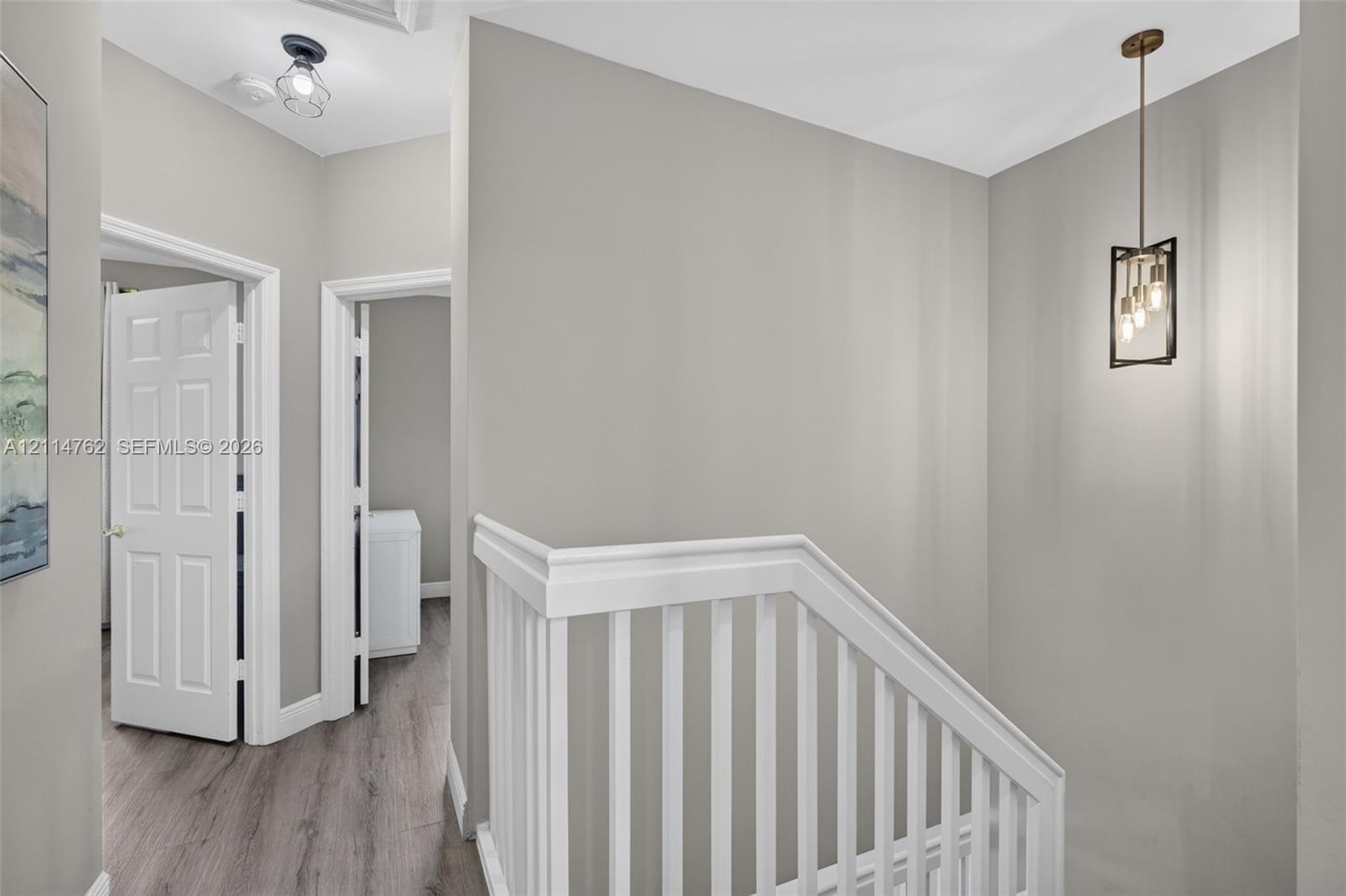 Hallway featuring wood-finish flooring, a white wooden balustrade, and a metal-framed geometric pendant light fixture