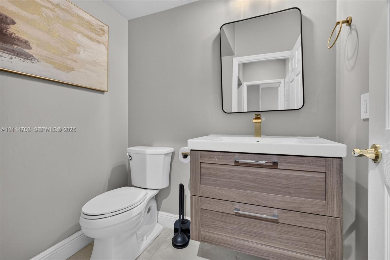 Floating wood-finish vanity with an integrated white sink, gold-toned faucet, square wall-mounted mirror, and gold-toned towel ring