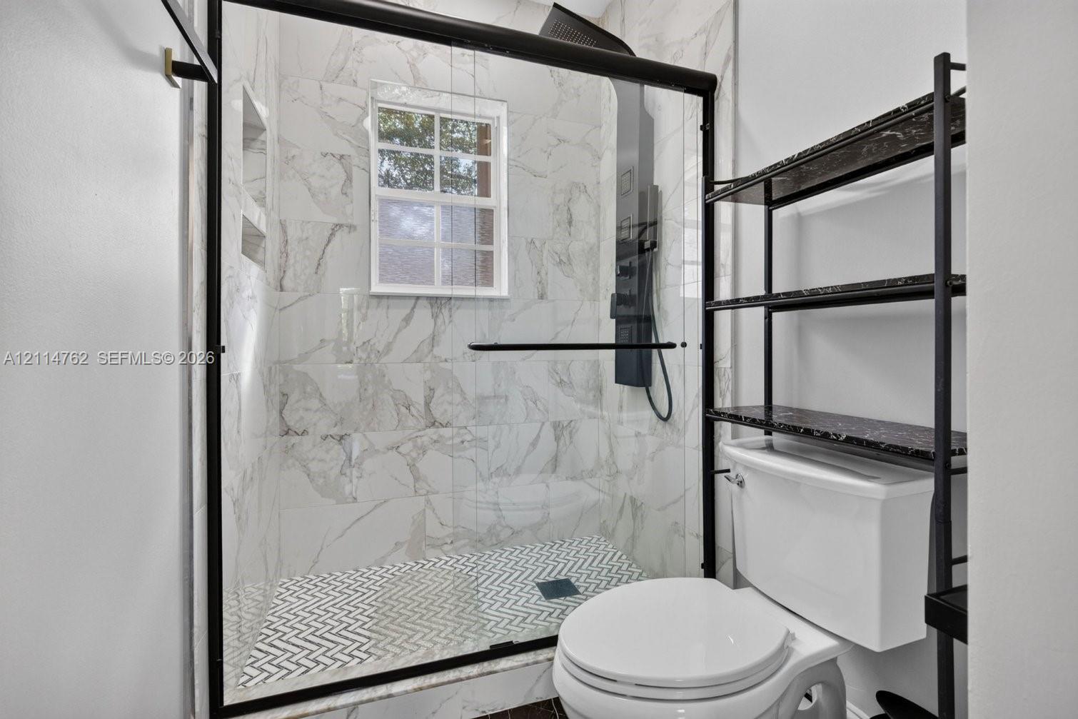 Walk-in shower featuring floor-to-ceiling stone-look tile, herringbone patterned tile flooring, a black-framed glass enclosure, and a built-in recessed wall niche