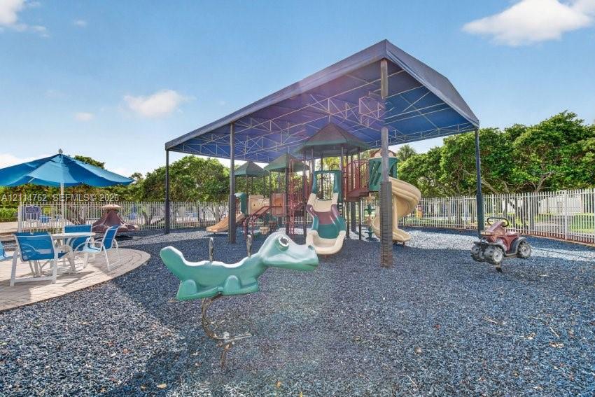 Recreational area featuring a covered playground structure with slides, integrated rocker equipment, and a perimeter metal fence