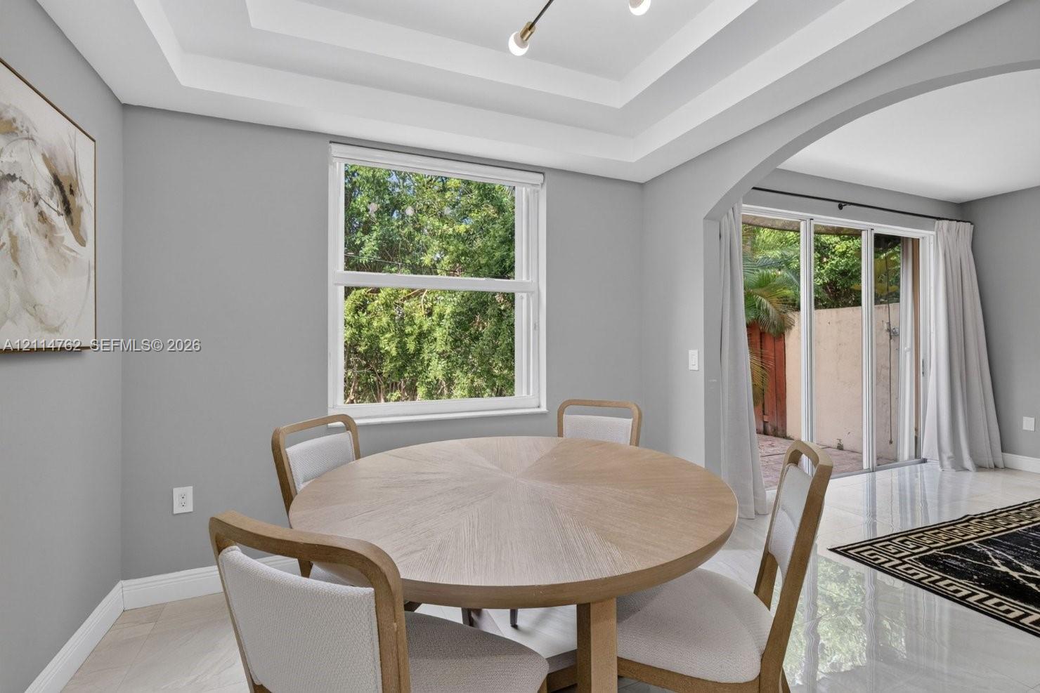 Tray ceiling with recessed lighting, arched entry, single-hung window, and glass sliding doors featuring polished tile flooring