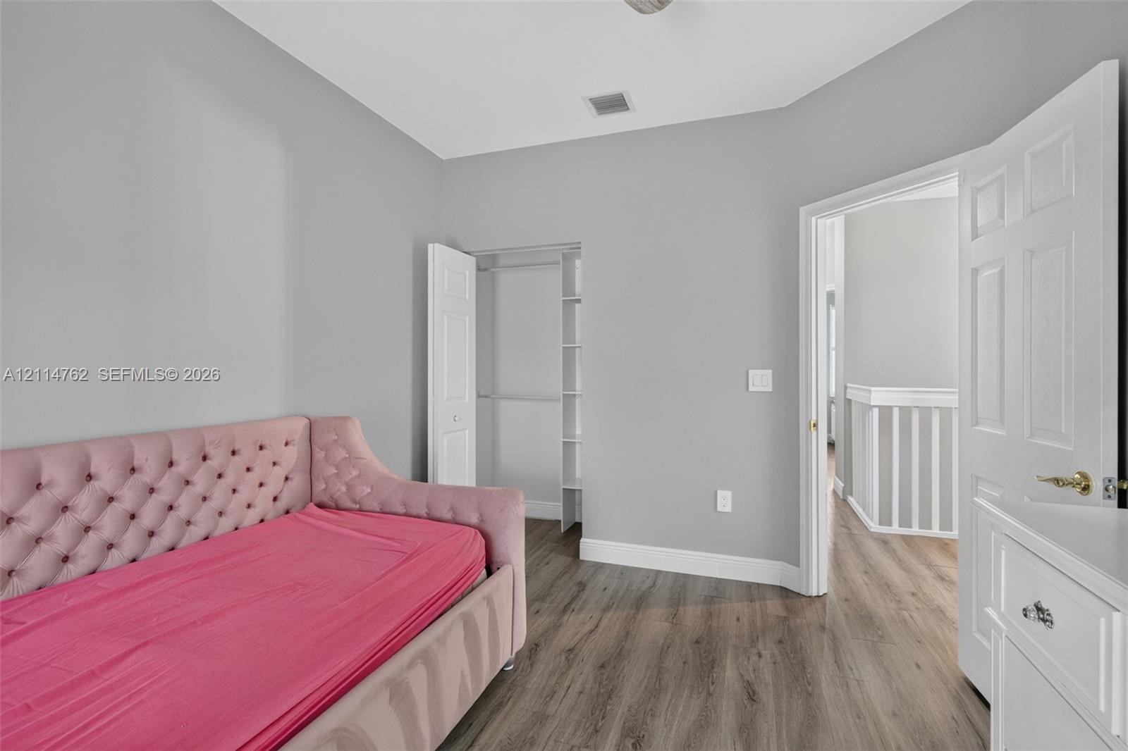 Neutral-toned interior featuring wood-finish flooring, a reach-in closet with built-in shelving, and white six-panel interior doors