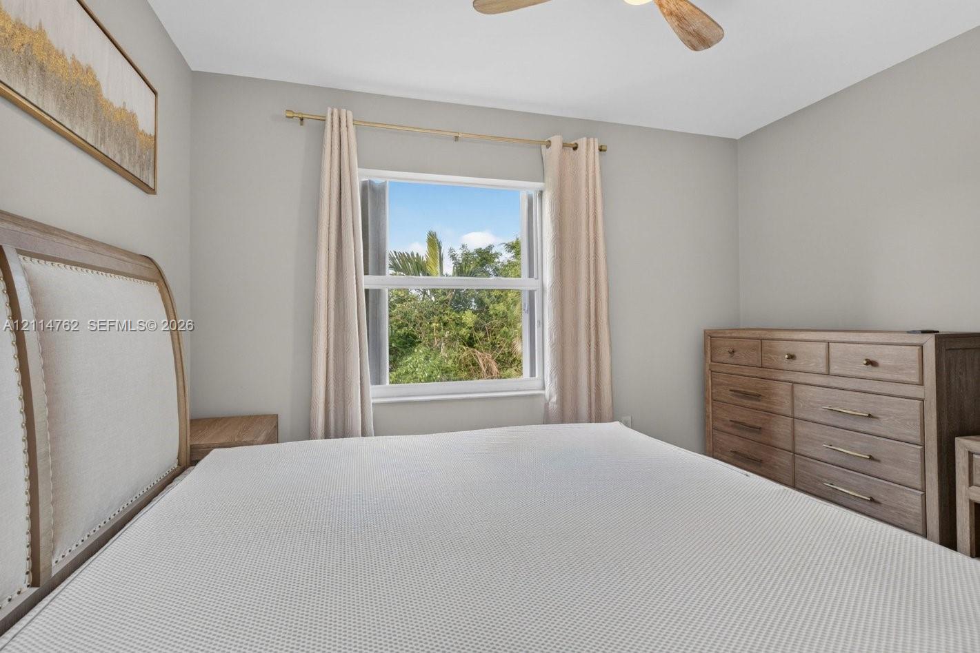 Neutral wall palette featuring a centered window with metallic rod hardware and a ceiling-mounted fan with wood-finish blades