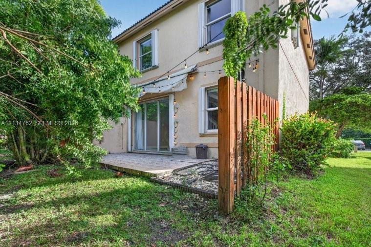 Stucco exterior featuring a paved patio, retractable awning, wood privacy fencing, and sliding glass doors