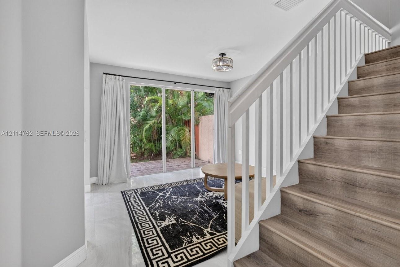 Interior featuring wood-finish staircase treads with white balusters, polished tile flooring, and glass sliding doors