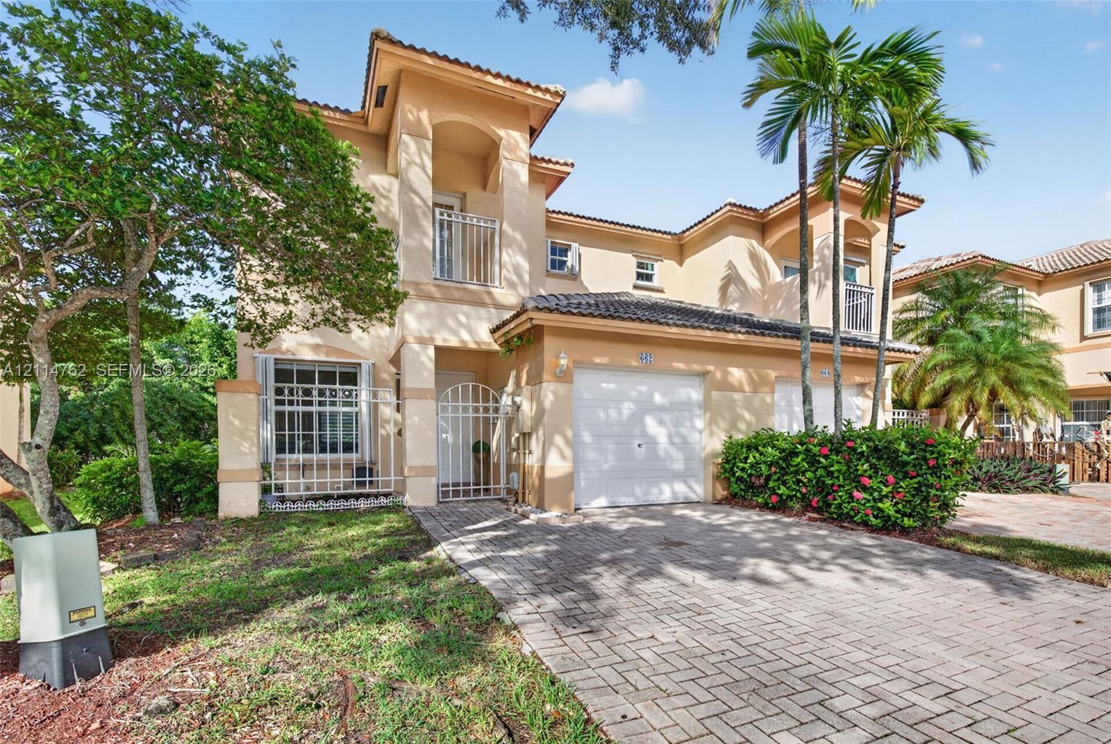 Two-story stucco exterior featuring a paved driveway, tile roof, gated courtyard entry, and integrated dual-car garage