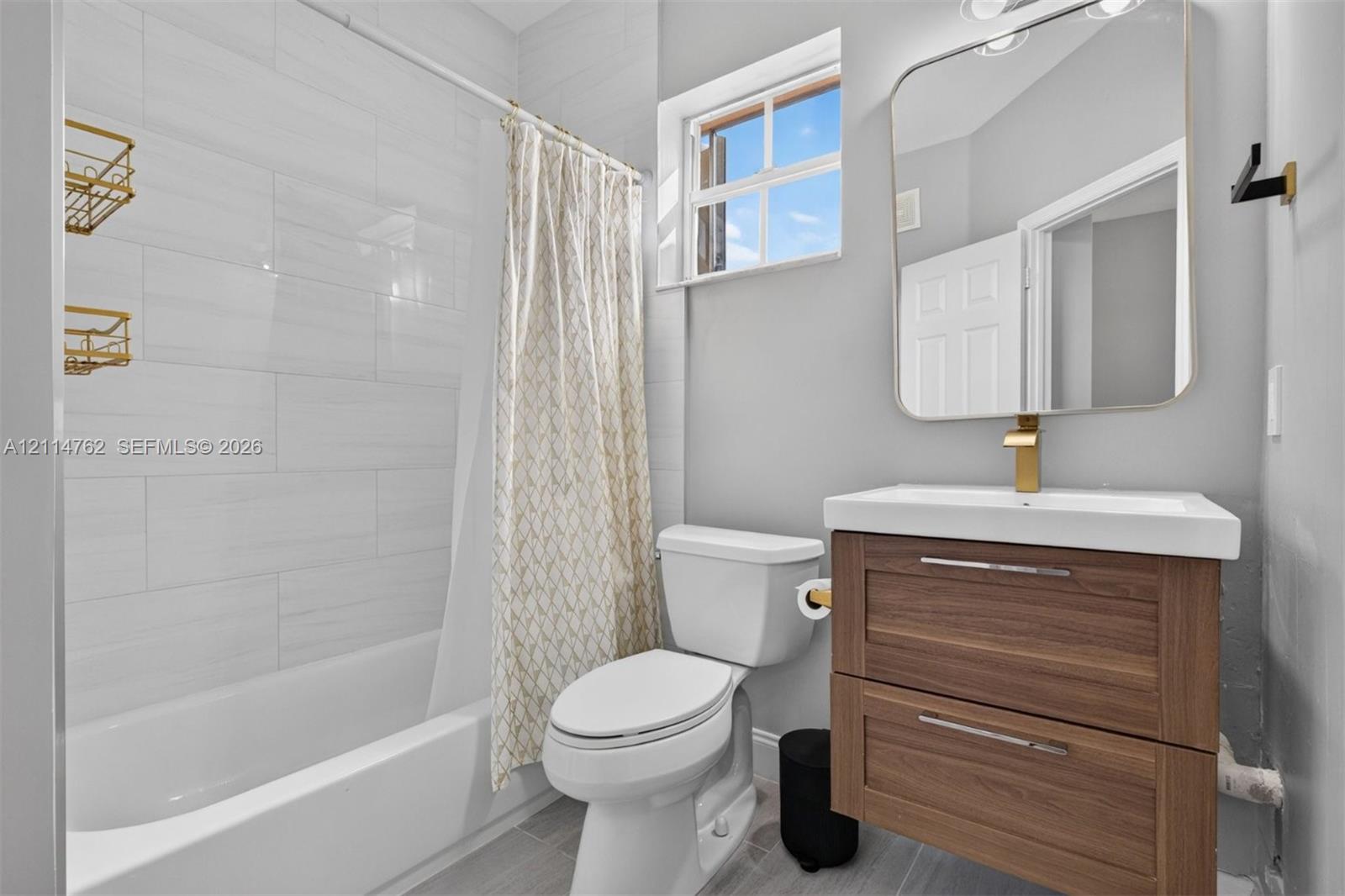 Bathroom featuring a wood-finish floating vanity, rectangular vessel sink, brass-tone hardware, and a tub enclosure with horizontal wall tile