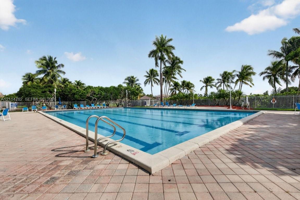 Large swimming pool featuring multi-lane lap markers, stainless steel handrails, and a surrounding paver patio lined with mature palm trees