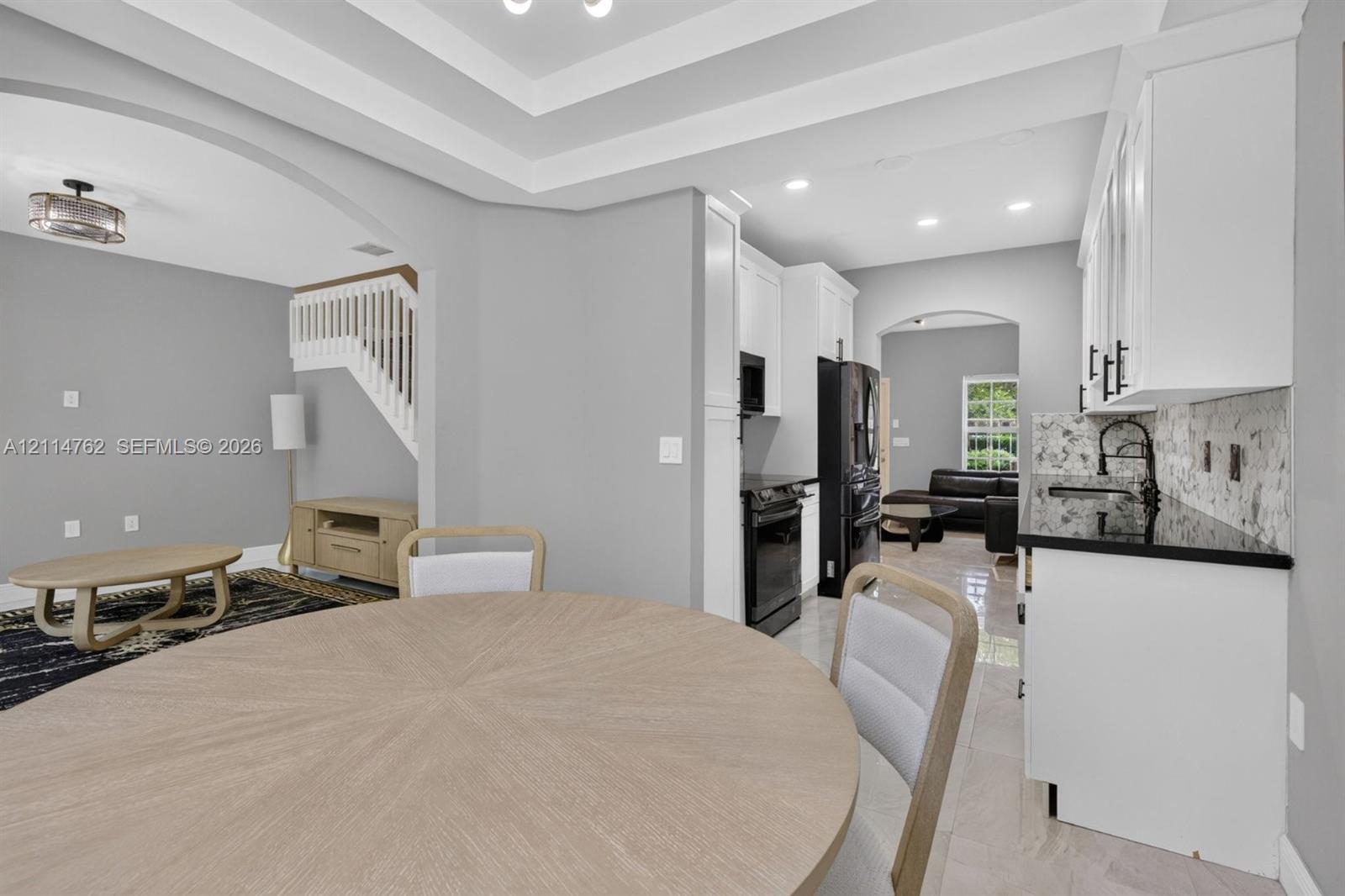 Kitchen featuring white cabinetry, black stone countertops, matte black hardware, recessed lighting, and tray ceilings