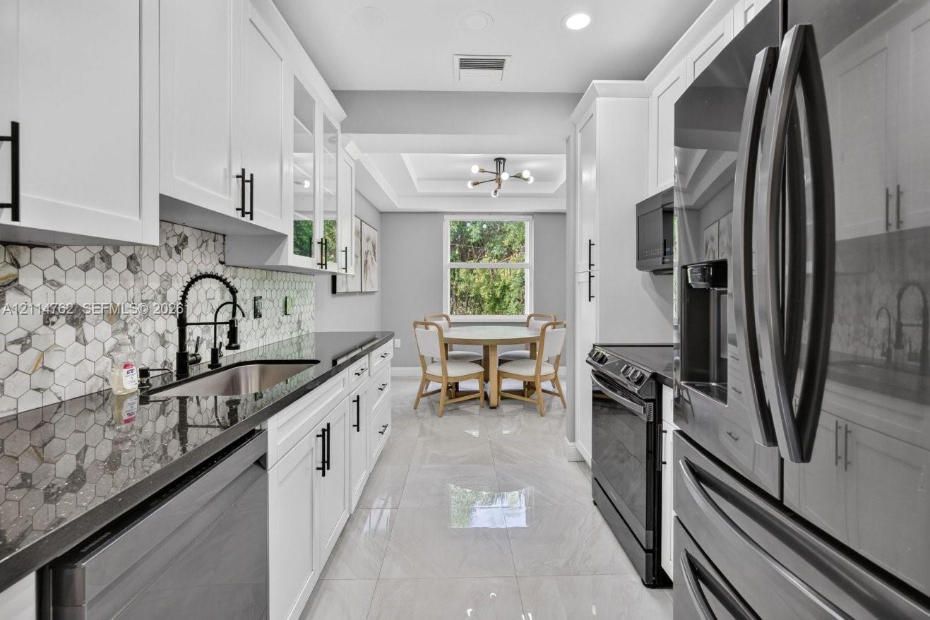 Kitchen featuring white Shaker-style cabinetry, dark stone-finish countertops, geometric tile backsplash, stainless steel appliances, and tile flooring