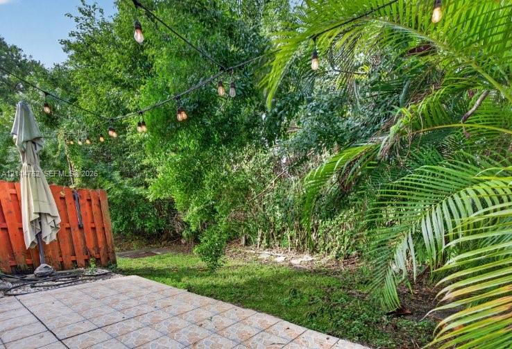 Outdoor patio featuring tiled flooring, a vertical wood fence, and string lighting