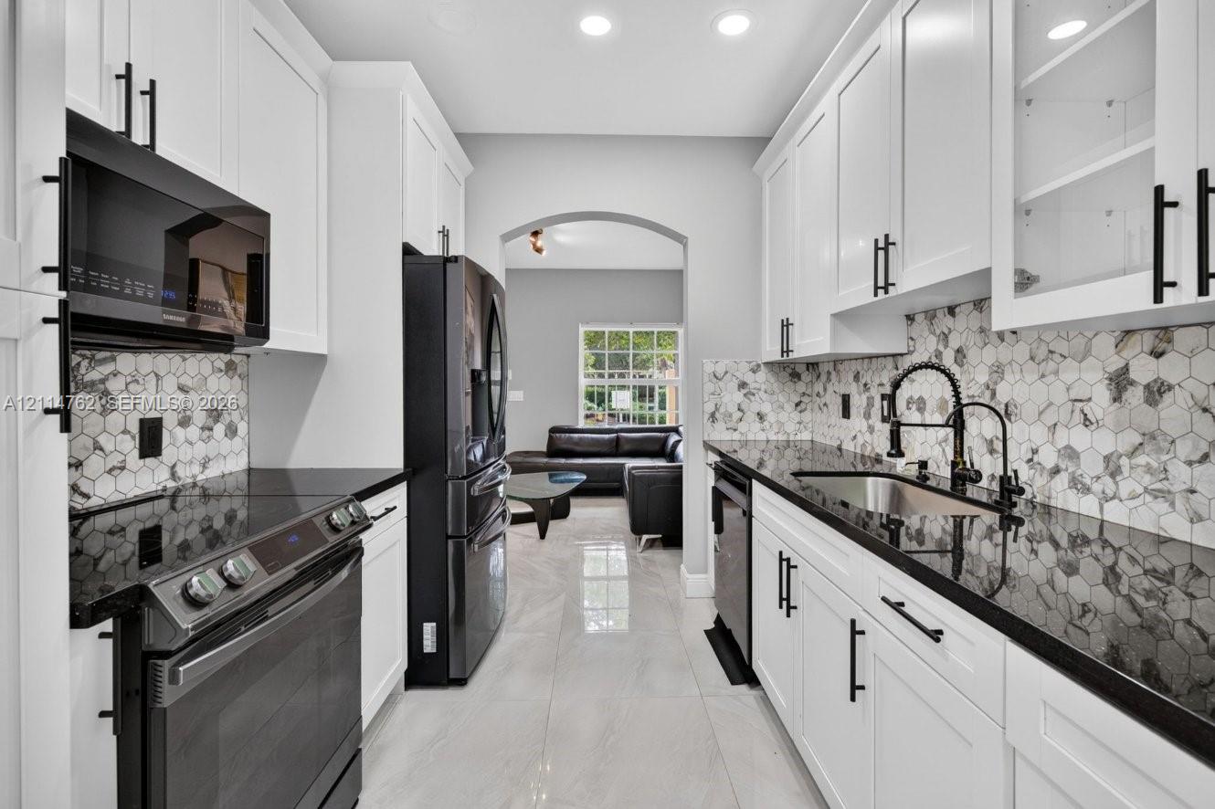 Kitchen featuring white cabinetry with matte black hardware, dark stone countertops, geometric patterned tile backsplash, recessed lighting, and stainless steel appliances